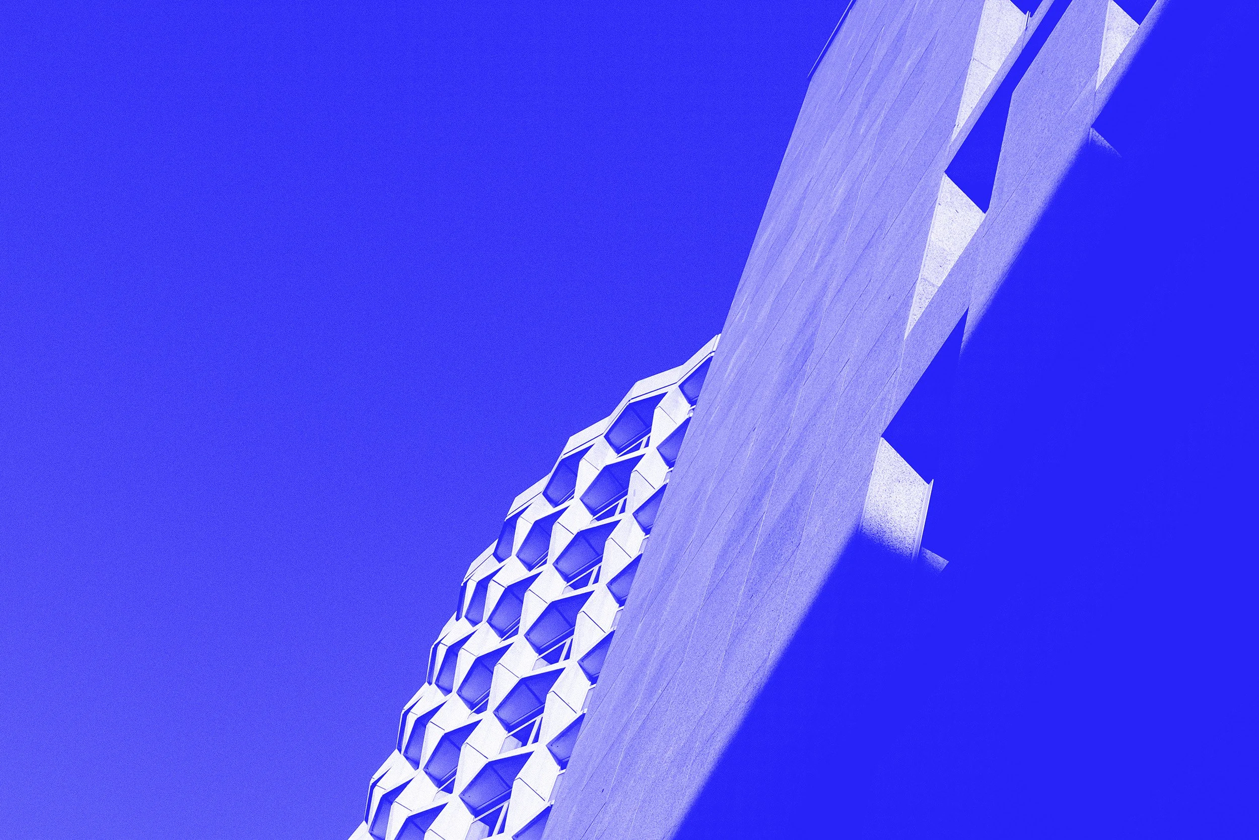 Close-up of a modern architectural building with a honeycomb-like pattern on one side, set against a clear blue sky.