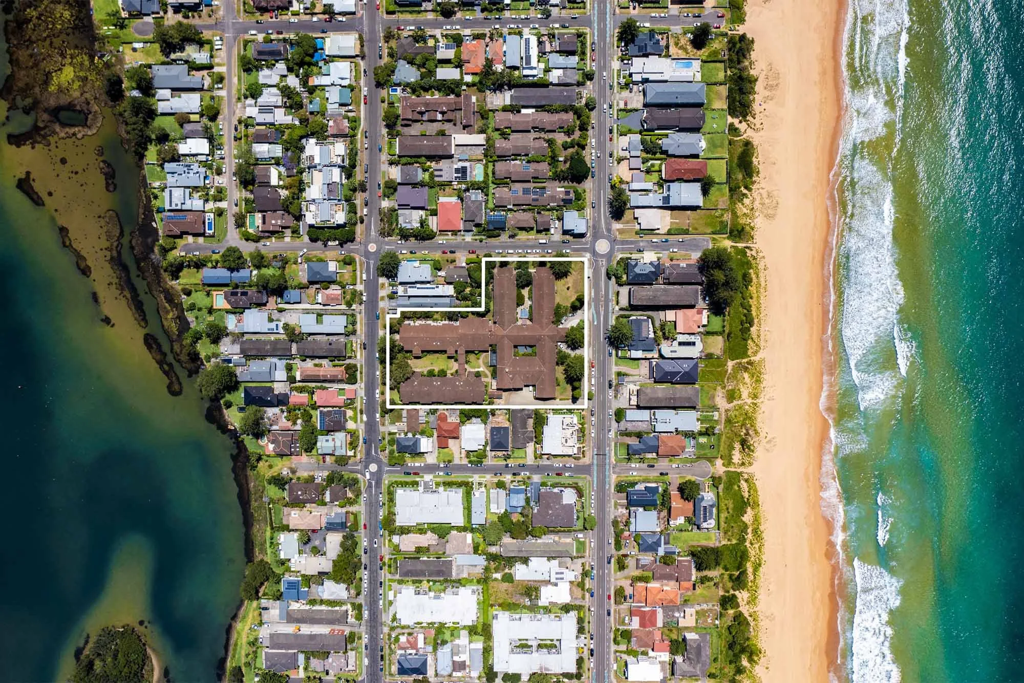 Aerial view of a coastal neighborhood with houses, streets, and a beach with waves on the right side.