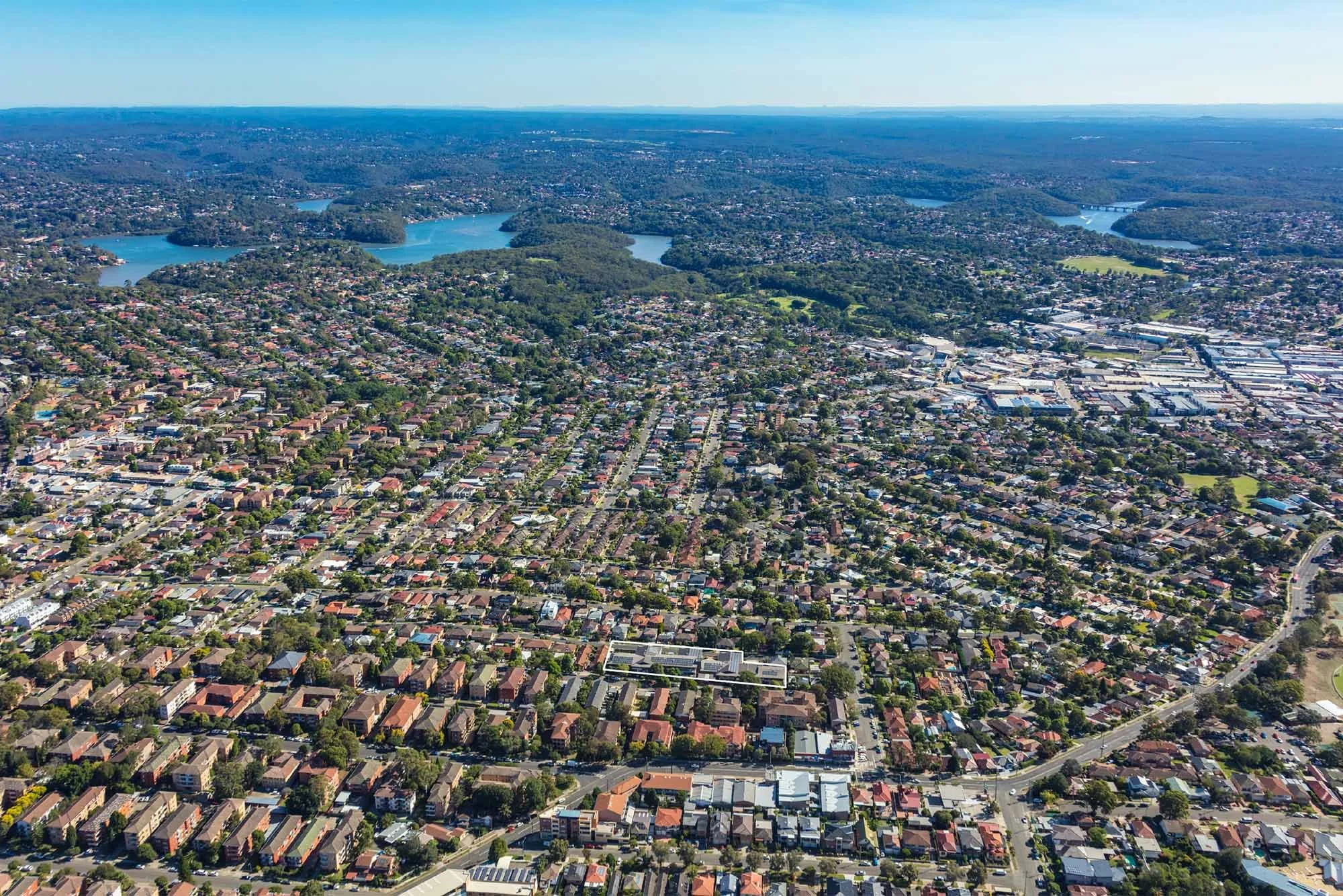 Aerial view of a suburban area with residential houses, roads, and green spaces, along with lakes and a cityscape in the distance.