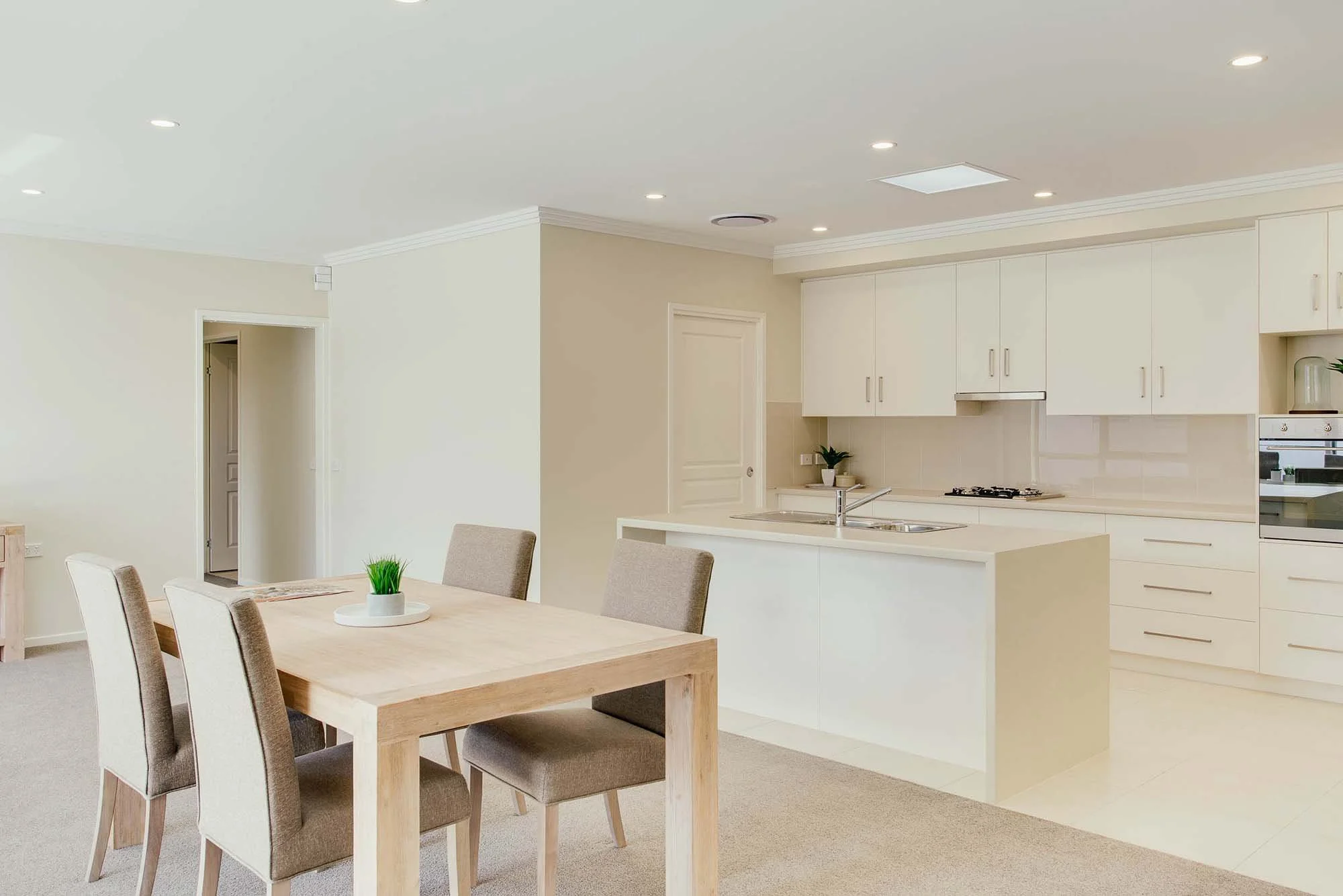 Bright and minimalist kitchen with white cabinets, beige walls, and a dining table with four chairs, decorated with a small green plant.