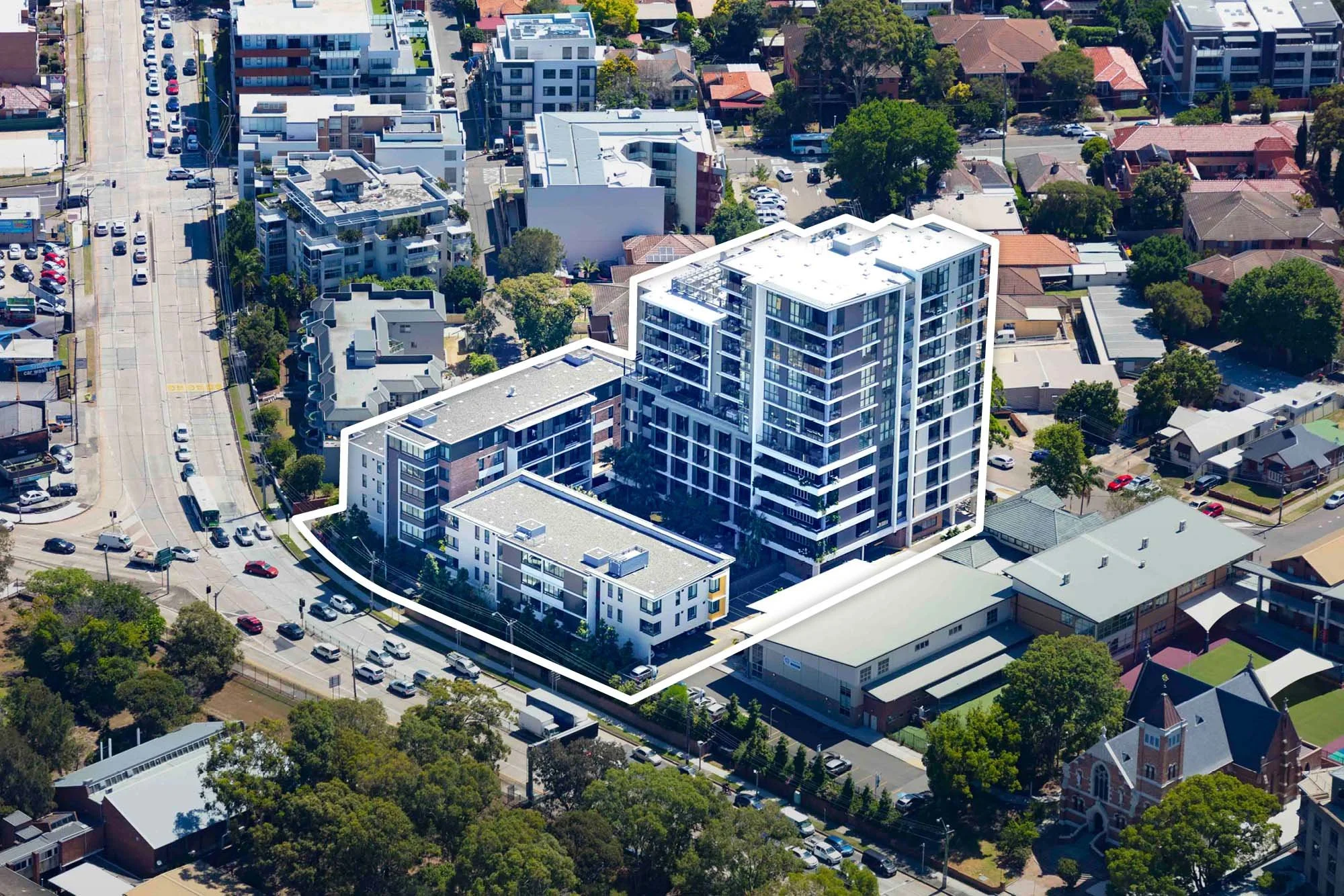 Aerial view of a mixed-use urban area showing modern apartment buildings, mid-rise residential structures, streets with parked cars, and surrounding trees.