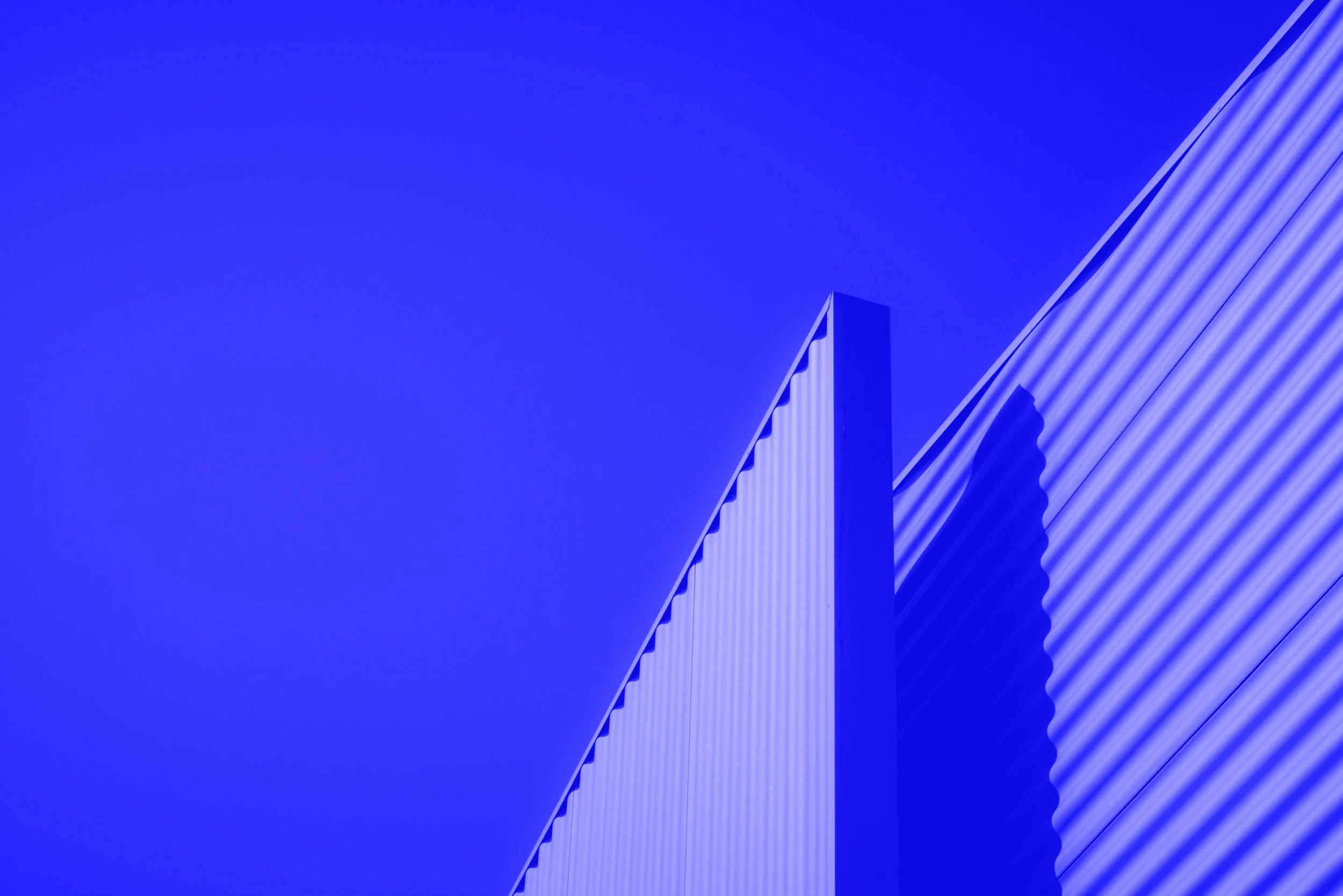 Close-up of a modern building with reflective, ribbed metal panels against a clear blue sky.