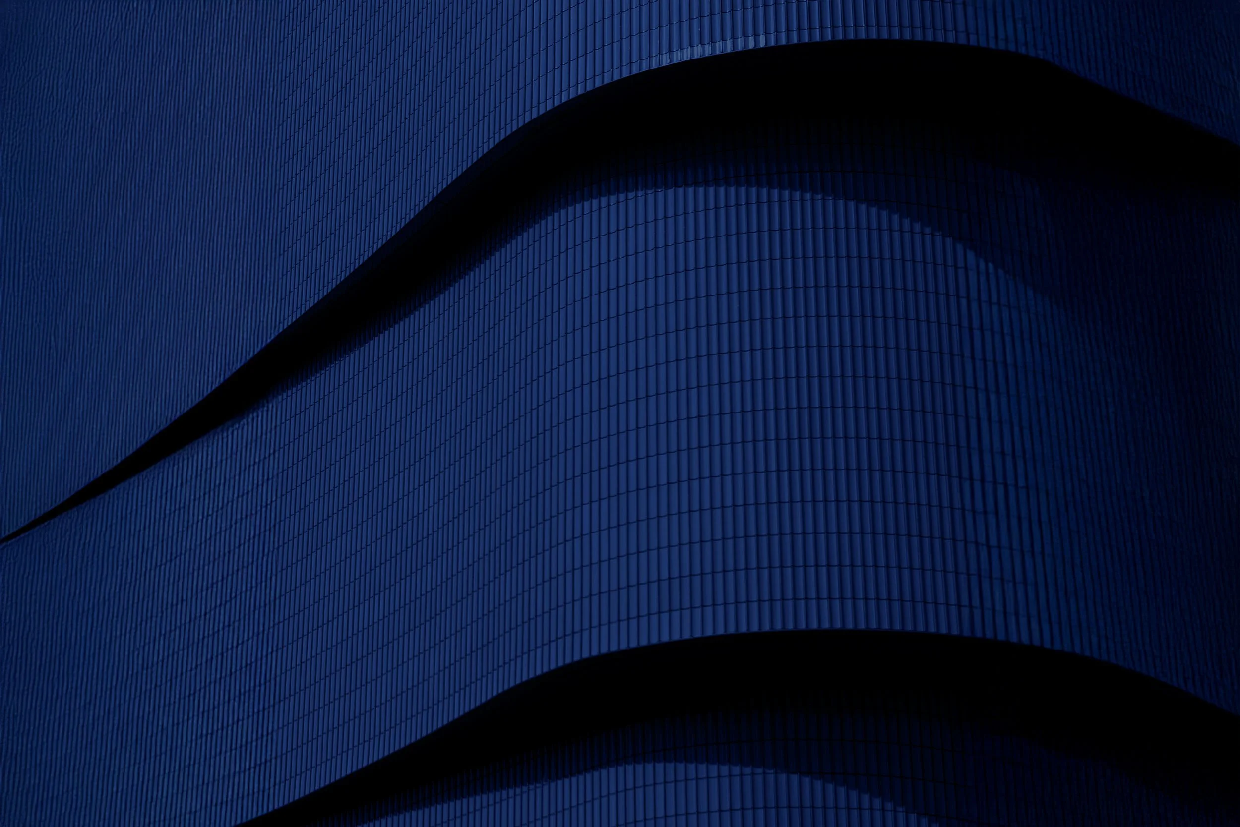 Close-up of a modern, curved building facade with dark blue tiles, emphasizing its architectural design.