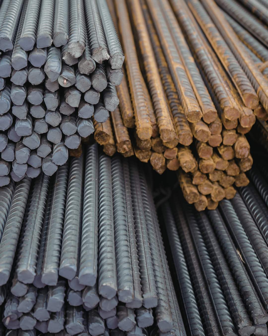 Stacks of steel rebar in metallic gray and rusty brown colors, arranged in bundles for construction.