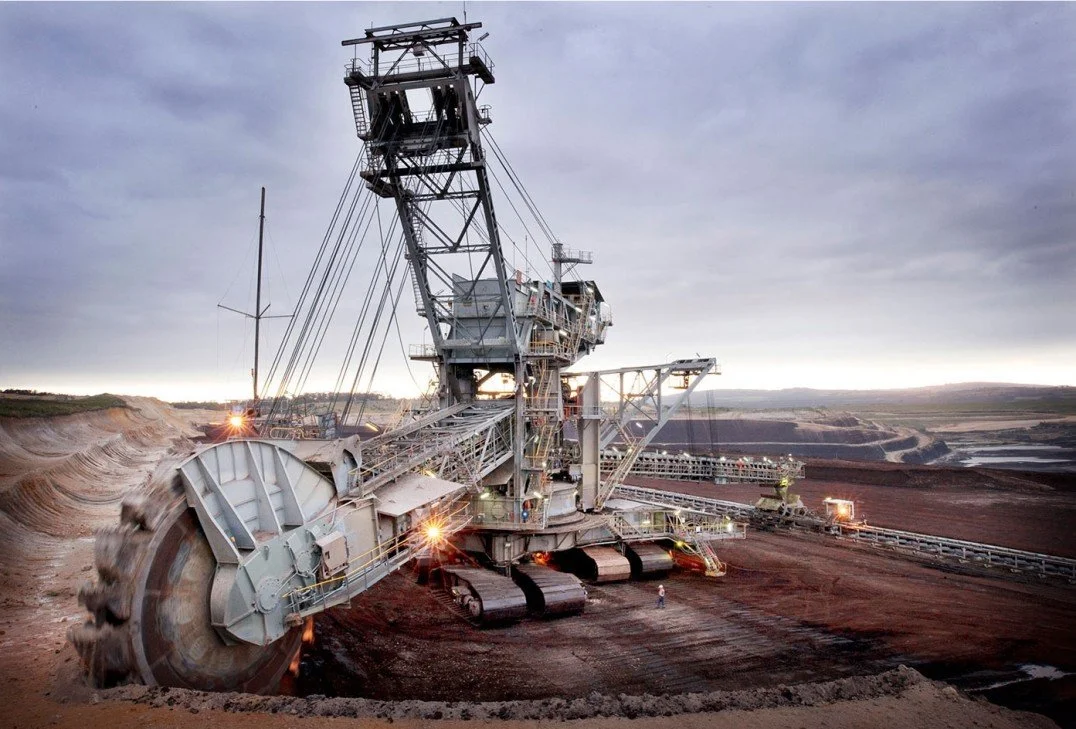 Large bucket wheel excavator working in an open-pit mine, with expansive earth and a cloudy sky in the background.