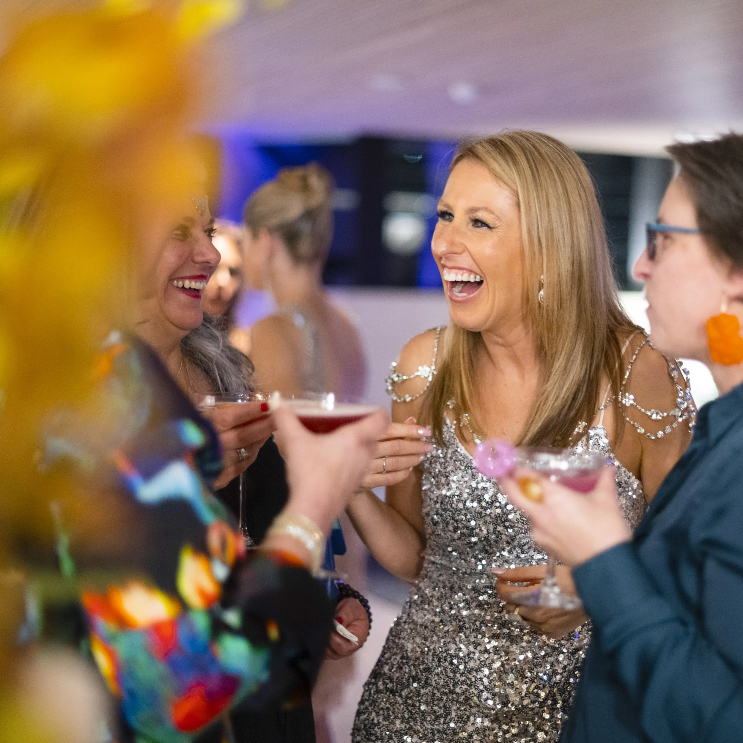Group of women having fun at a party, holding cocktails and laughing.