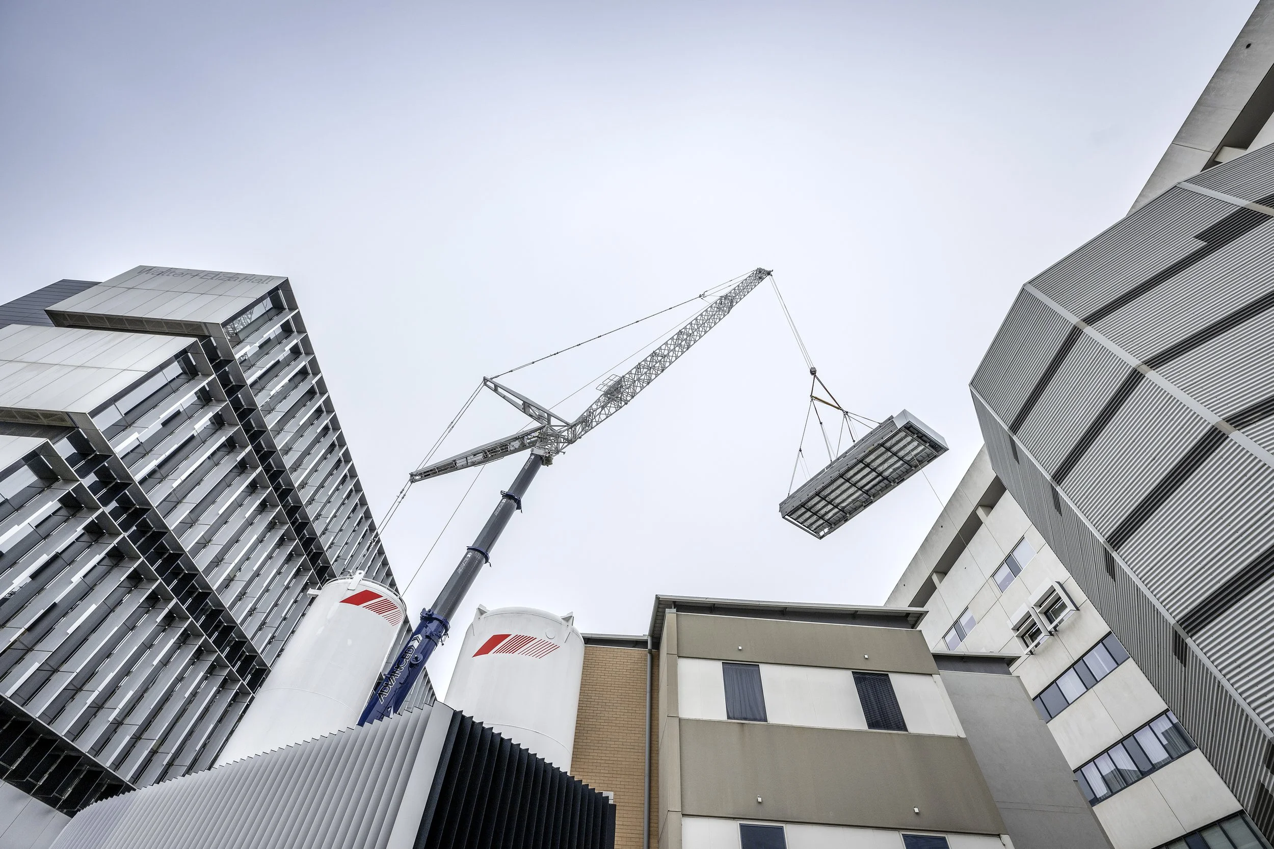 Construction crane lifting a building section in an urban construction site surrounded by modern high-rise buildings.