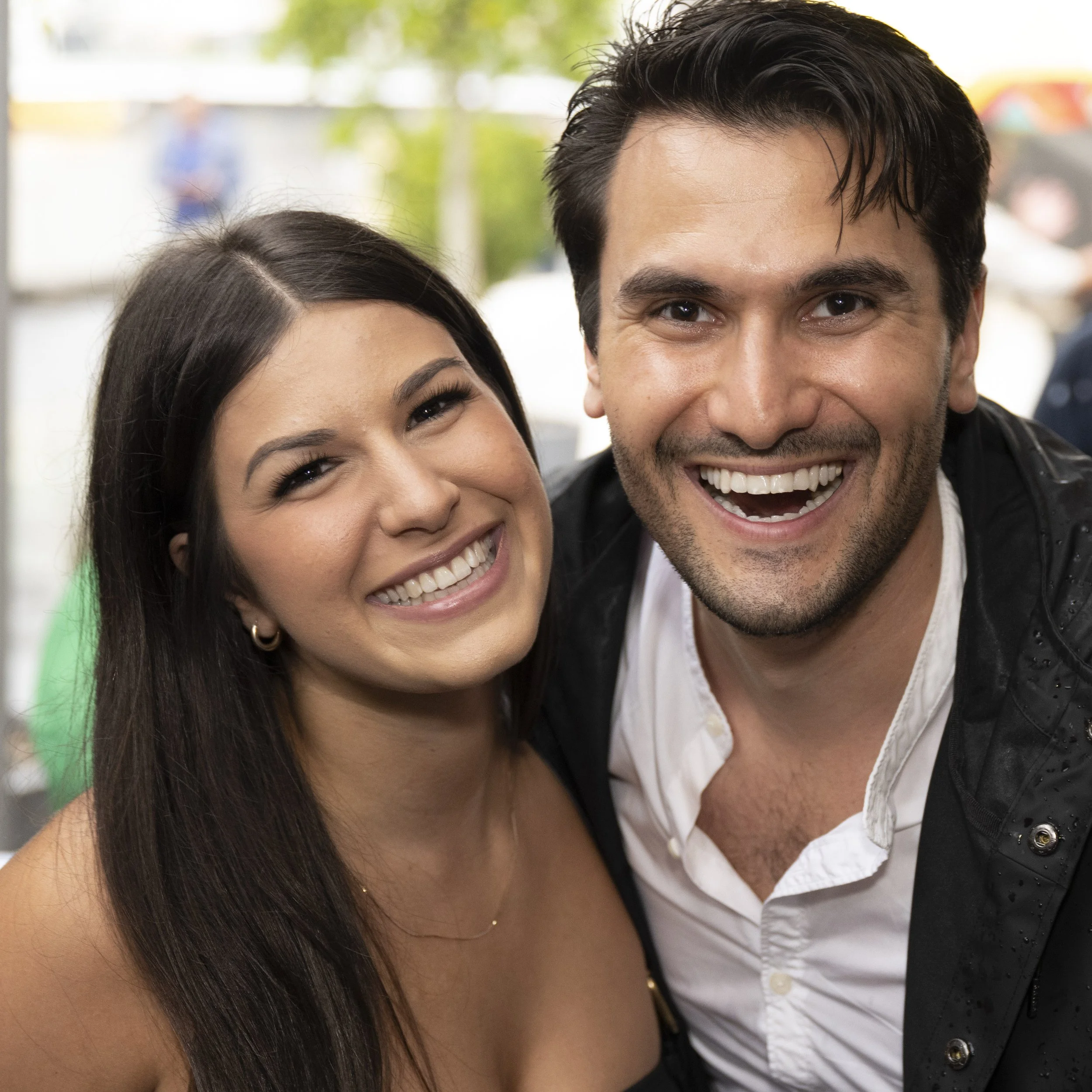 Close-up of a smiling man and woman with happy expressions, outdoors on a sunny day.