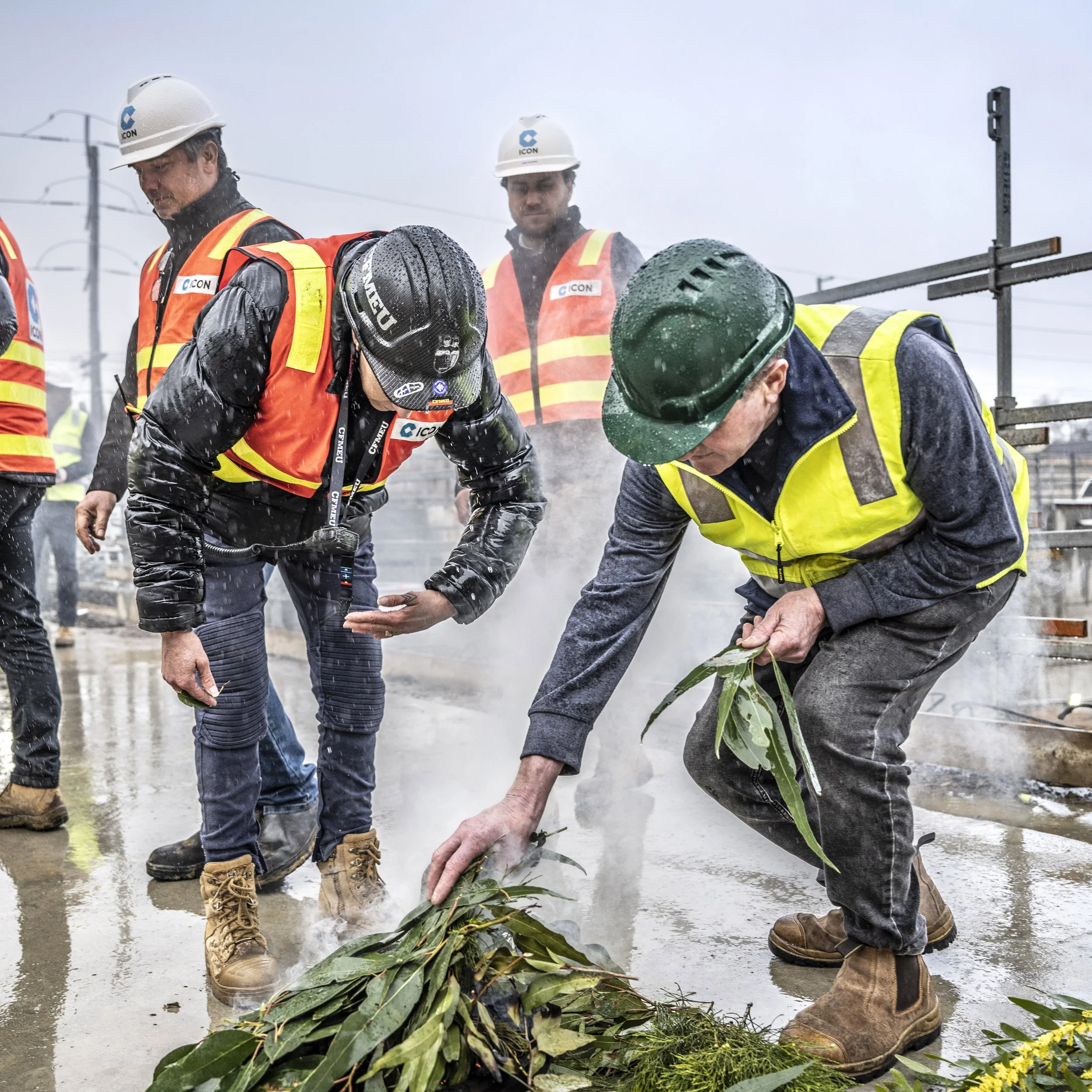 Construction workers in safety vests and helmets laying a plant on a wet construction site.