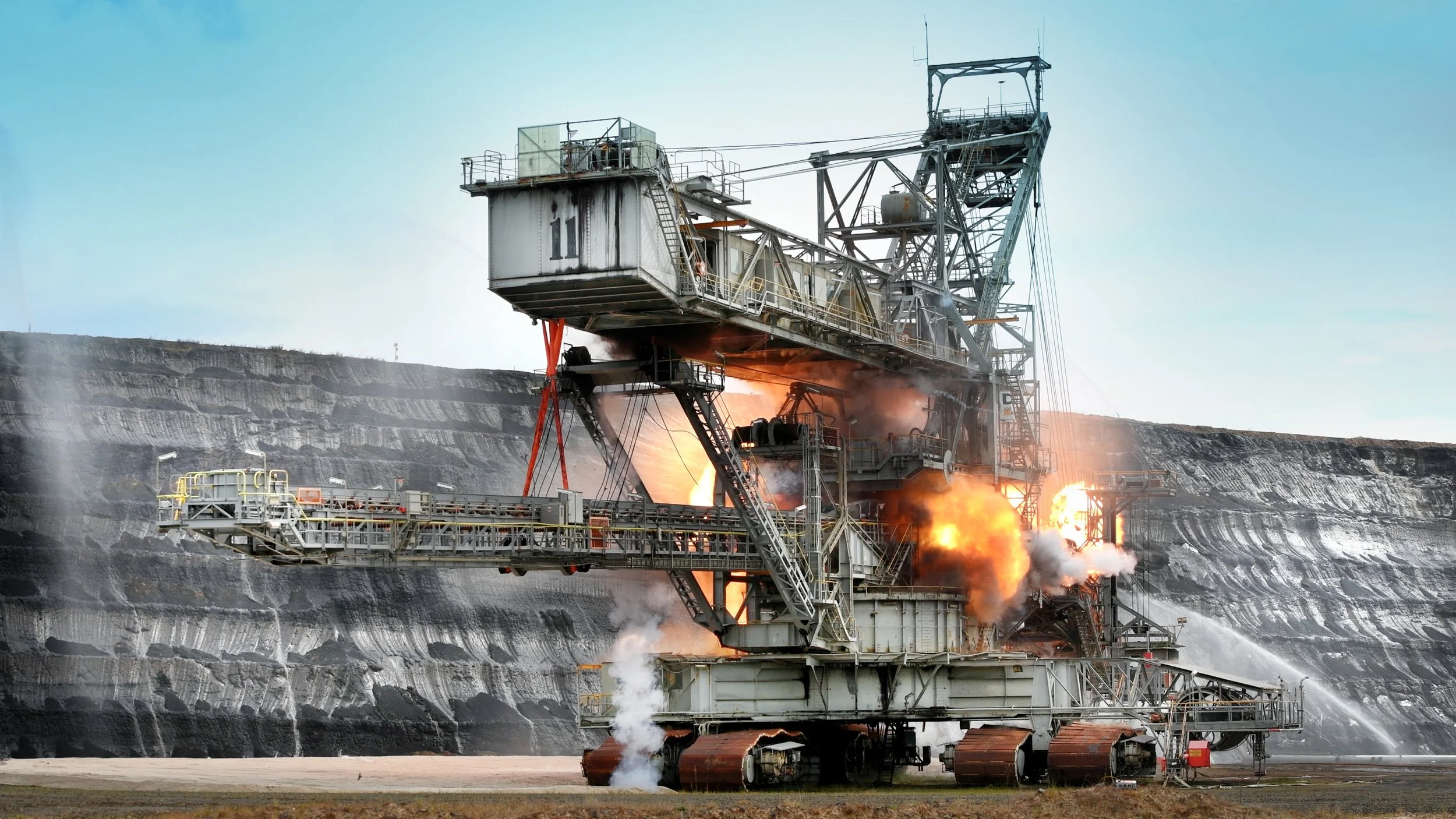 Large open-pit mining drill rig with sparks and flames, emitting smoke and lit up from the internal fire, working at the surface of a coal or mineral mine.