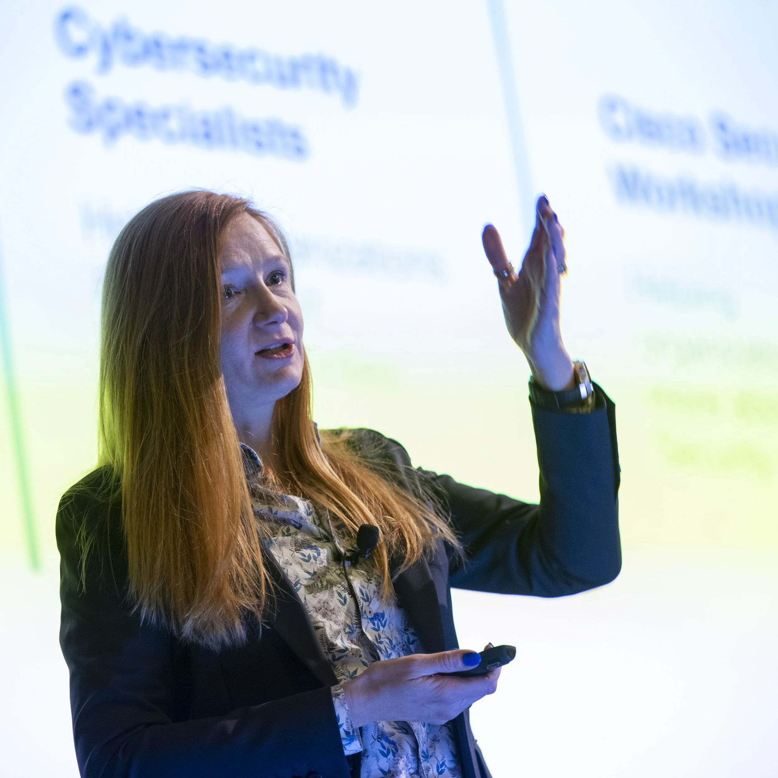Woman with long red hair giving a presentation in front of a slide with blue text.