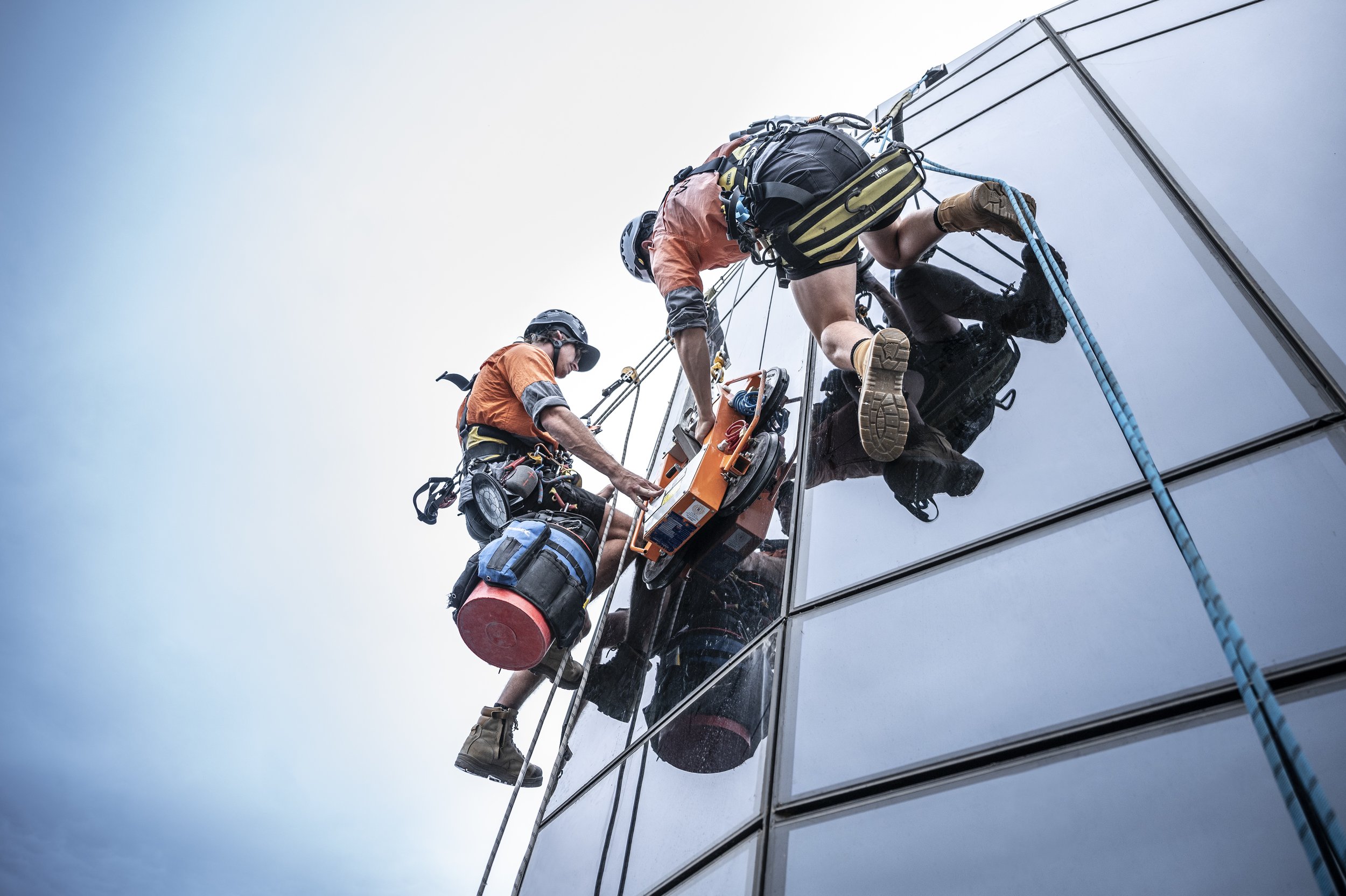 Two window washers cleaning the exterior windows of a tall building using a suspended scaffold.