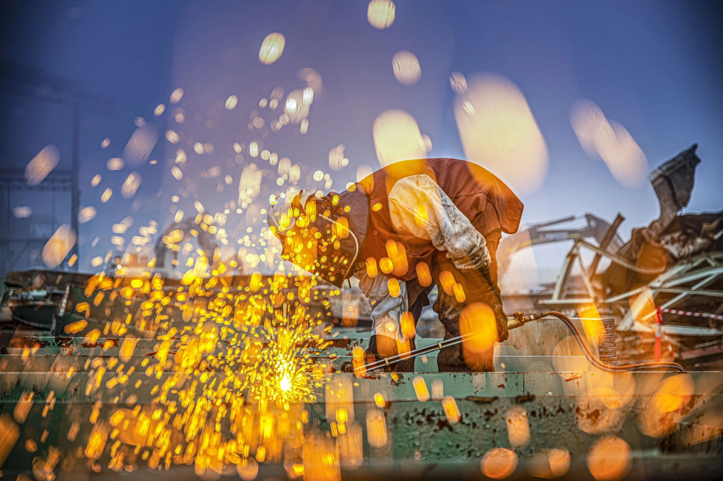 A worker welding metal with sparks flying in the air, wearing protective gear.
