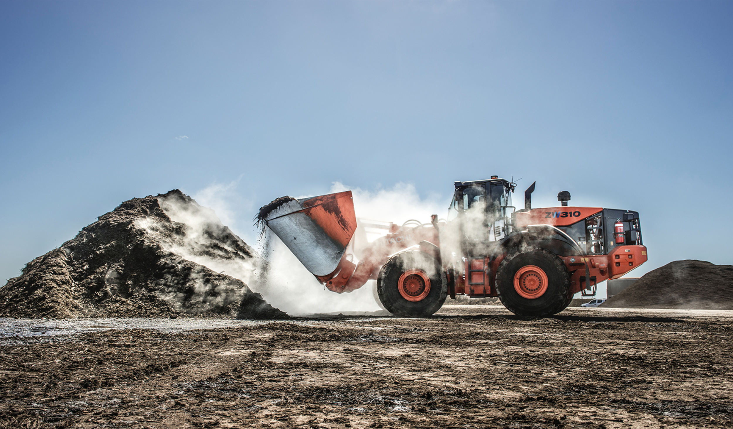 A large red bulldozer moving dirt on a construction site with a clear blue sky in the background.