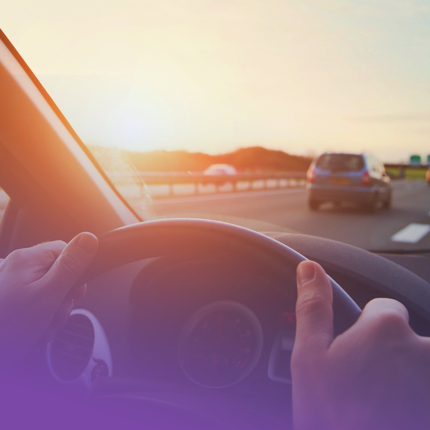 Driver's hands on steering wheel on a highway during sunset.