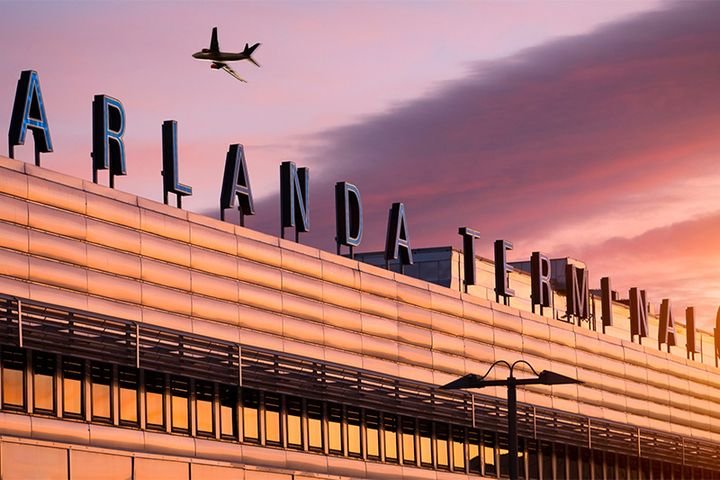 Flygplan flyger över Skyhall på Orlando International Airport vid solnedgång.