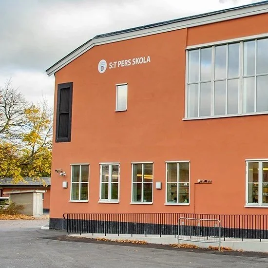 Skolbyggnad med orange fasad och skylt som säger 'St: PERS SKOLA'.