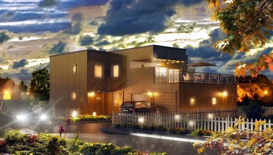 Moderne to-etasjes hus med utendørs balkong og opplyst hage om kvelden, under en dramatisk skyfarget himmel.