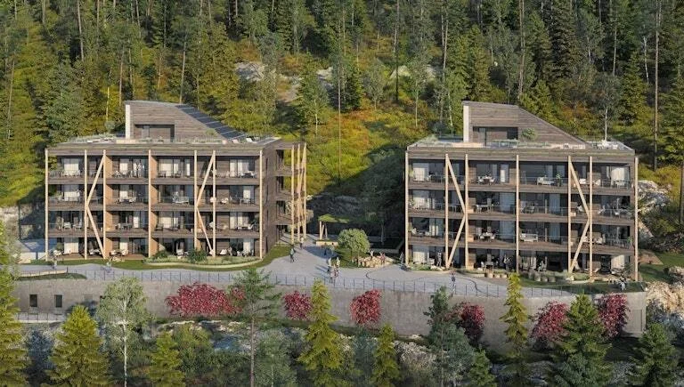 To moderne leiligheter byggd i tre, plassert på en skråning med en grønn skog i bakgrunnen.