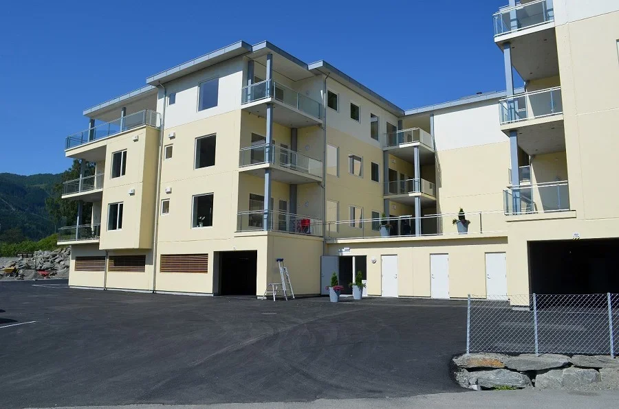 Fleretasjert boligblokk med flere balkonger og en parkeringsplass foran.