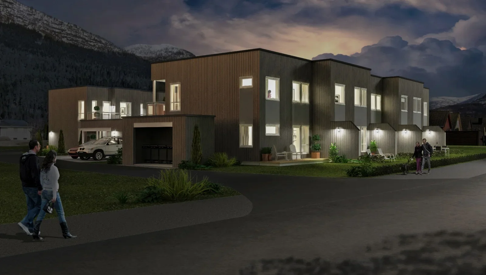 Nattbilde av moderne boligområde med opplyste hus, mennesker som går, og fjell i bakgrunnen.