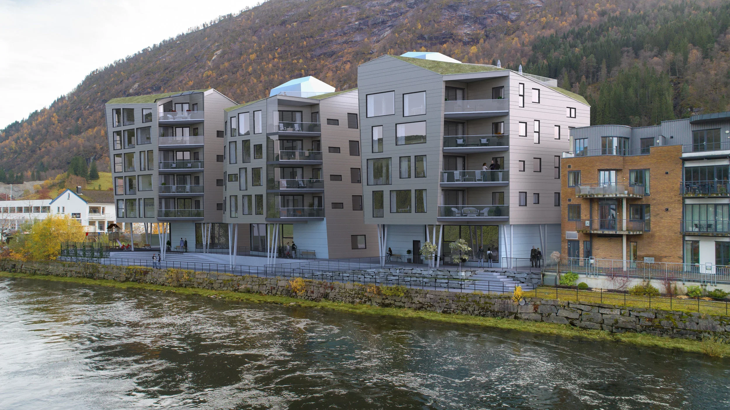 Fleretasjes moderne boligblokker ved en elv med fjell i bakgrunnen