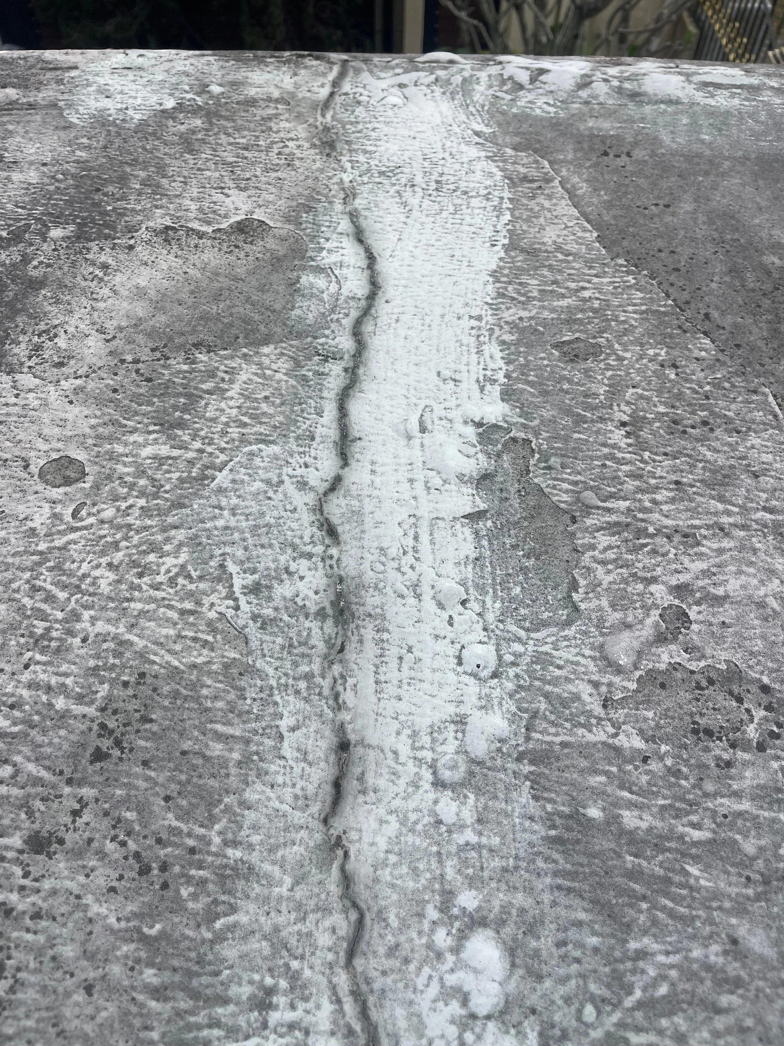Close-up of a concrete surface with a prominent crack and weathered white paint stripe running down the center.