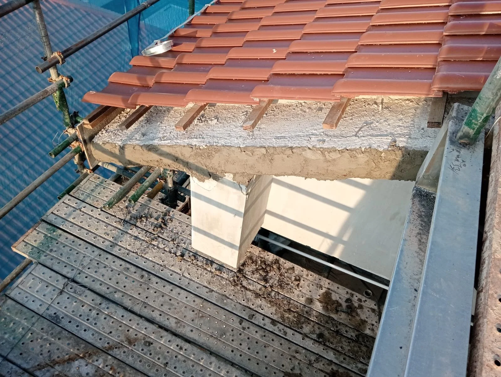 Roof under construction with scaffolding, red roof tiles, and exposed mortar and concrete structure.