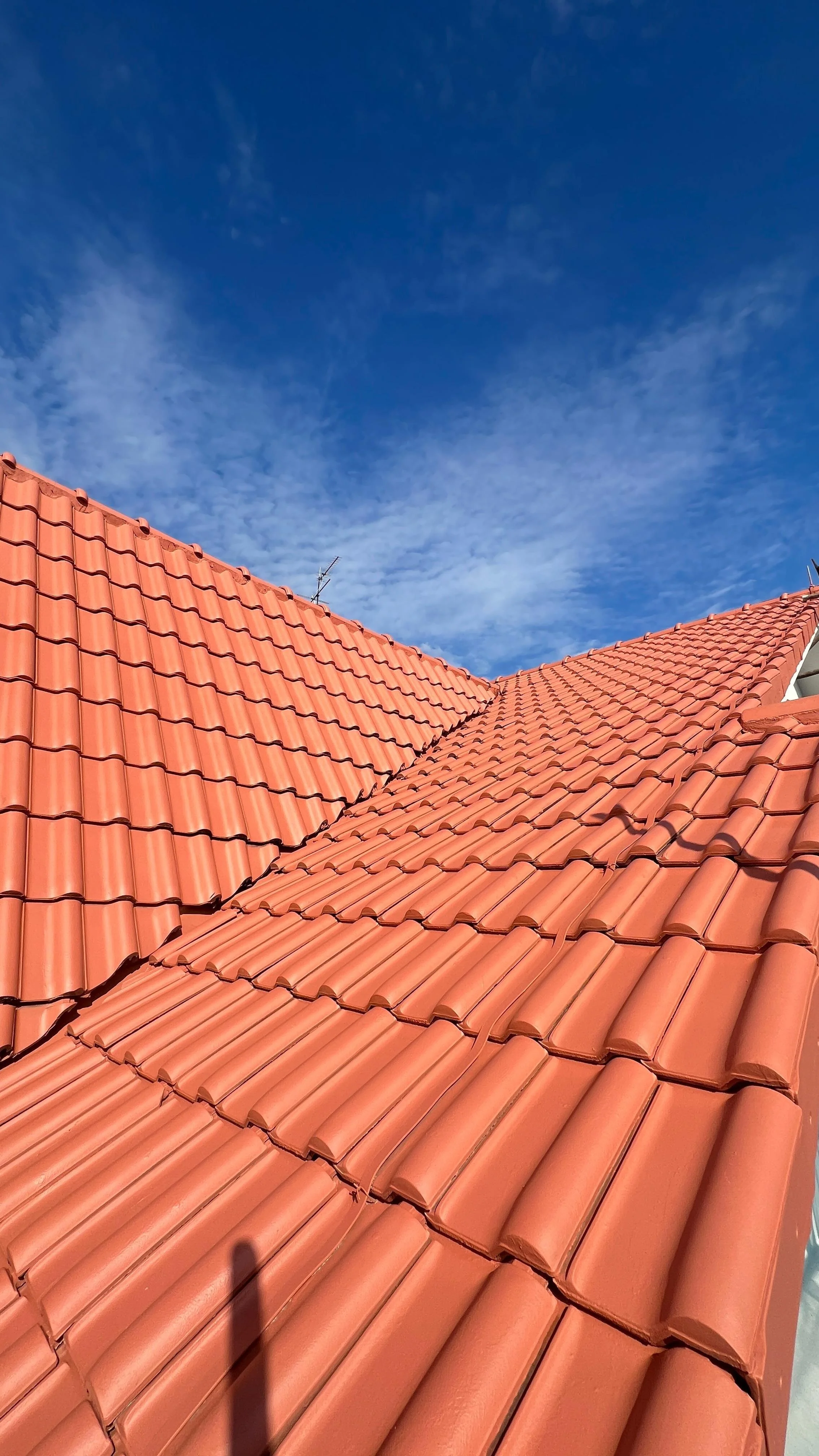 Close-up view of red clay tile roofing on a house with a bright blue sky in the background.