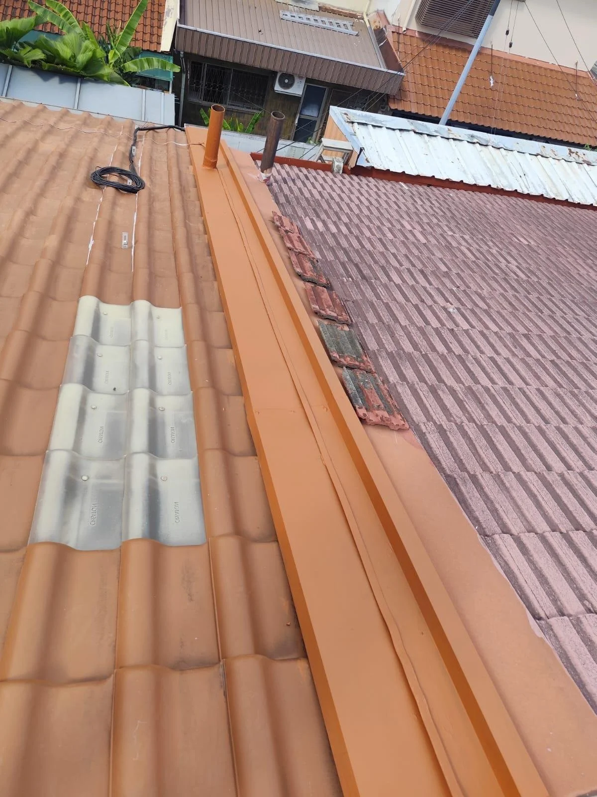 Roof with ongoing repair showing orange and tile roofing materials, metal flashing, and two pipes extending upward.