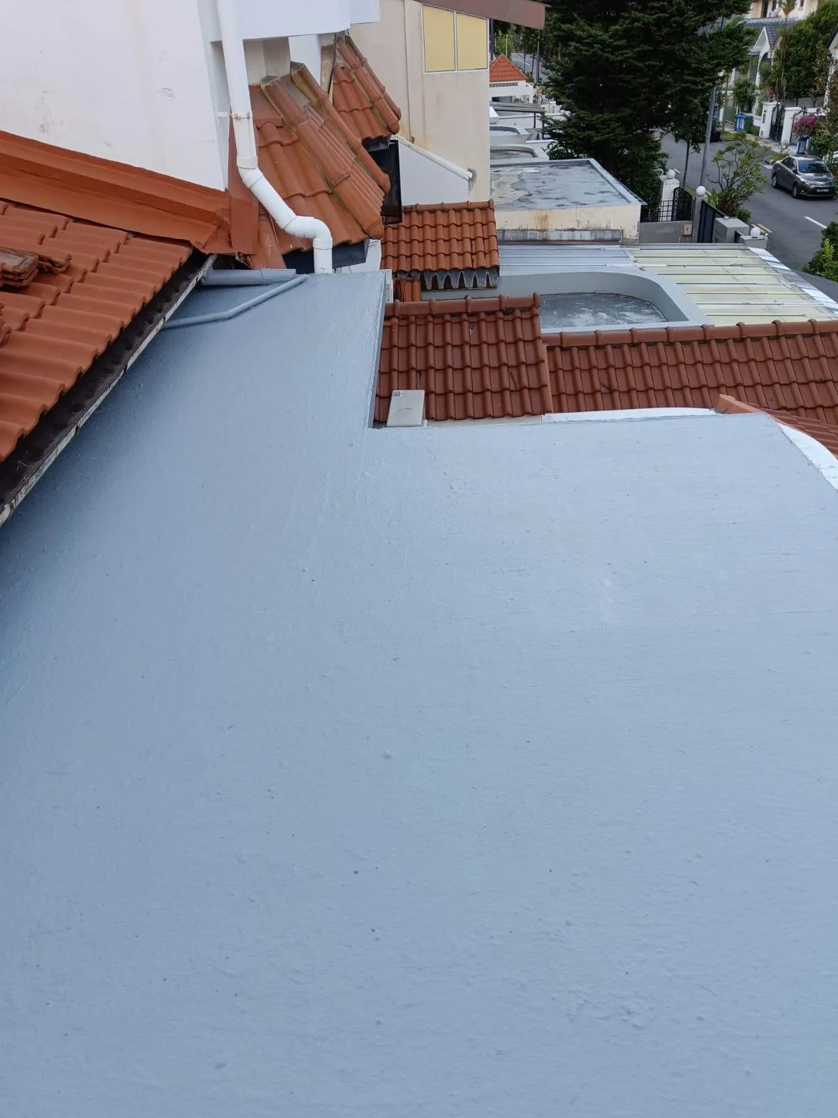 View of rooftops with red clay tiles and a prominent blue flat roof in an urban residential area, with streets and trees visible in the background.