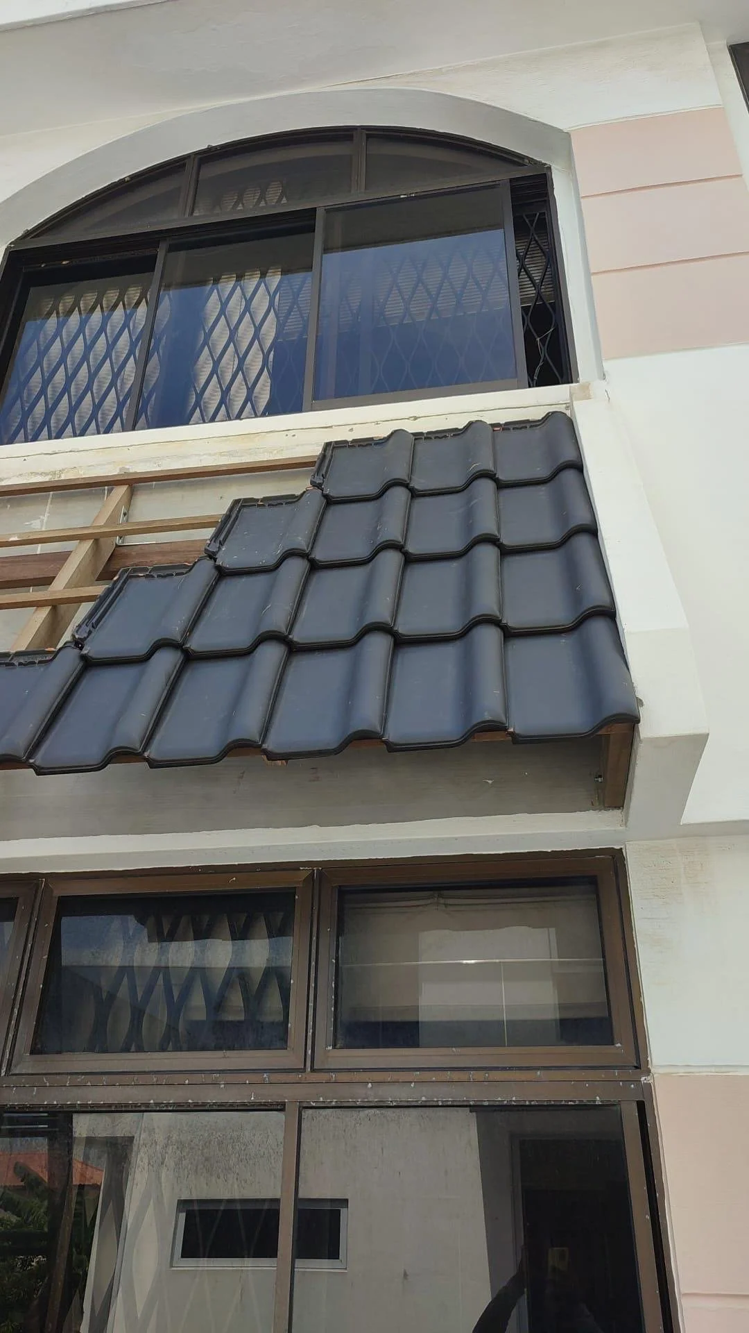 A building with large windows and a small tiled roof over the second floor window, along with a construction or repair wooden frame next to the window.