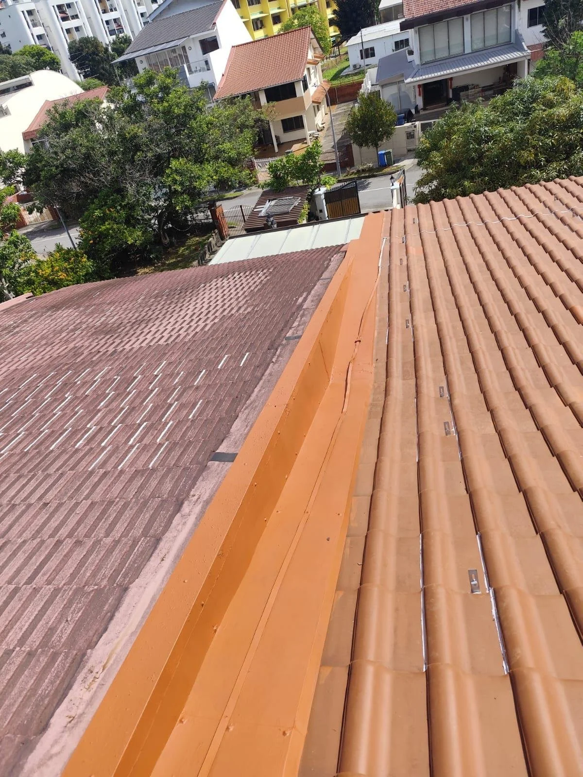 View of rooftops with different types of tiles, including clay and concrete, in a residential area with trees and houses in the background.