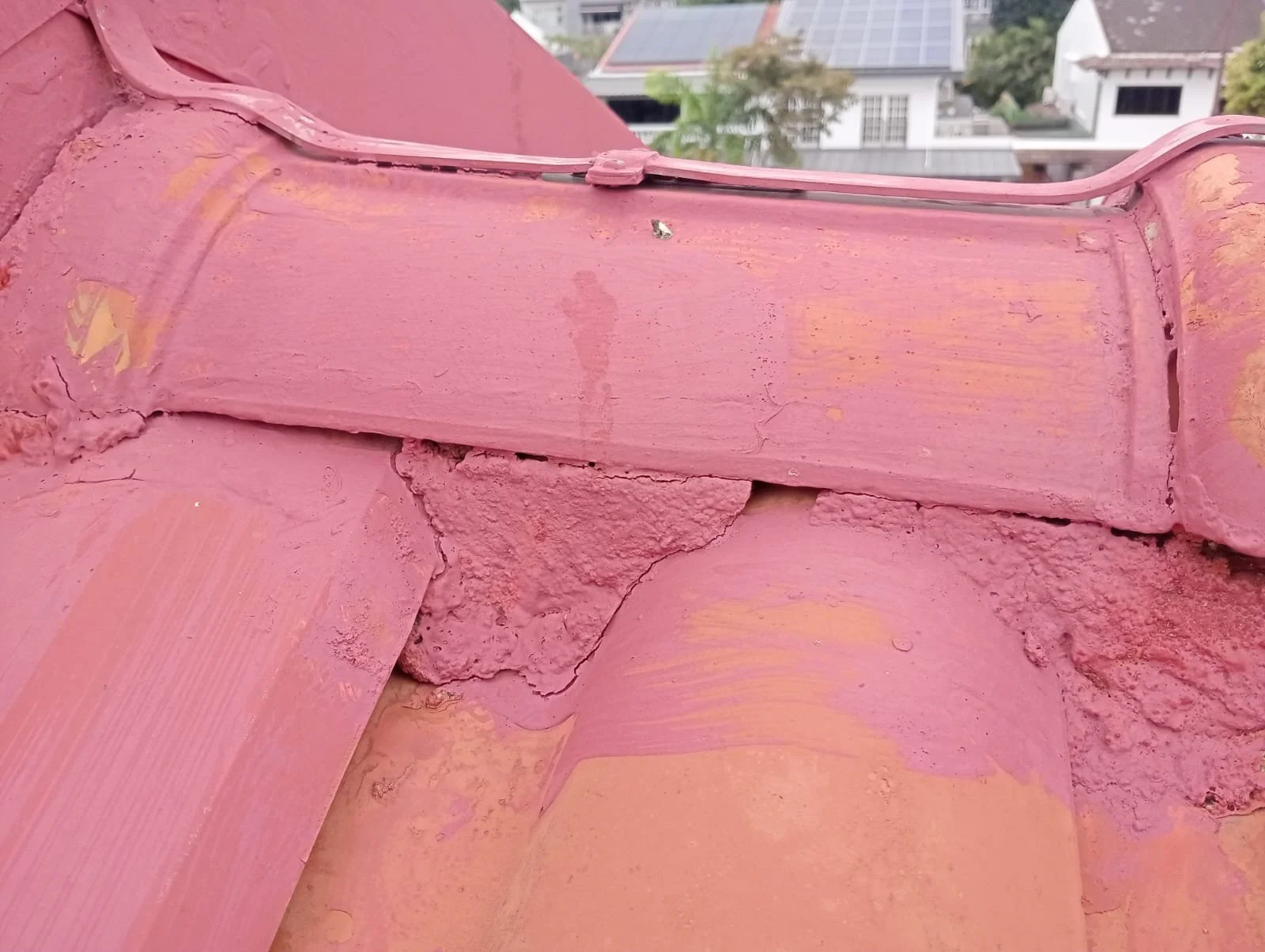 Close-up of a rooftop with pink painted tiles showing signs of peeling and damage.