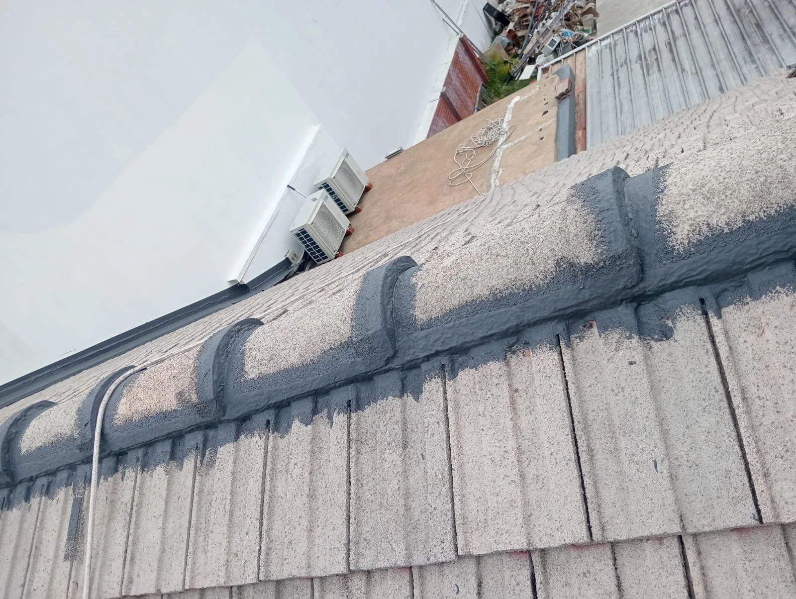 Close-up of a roof edge with freshly applied black sealant or coating on roof tiles.