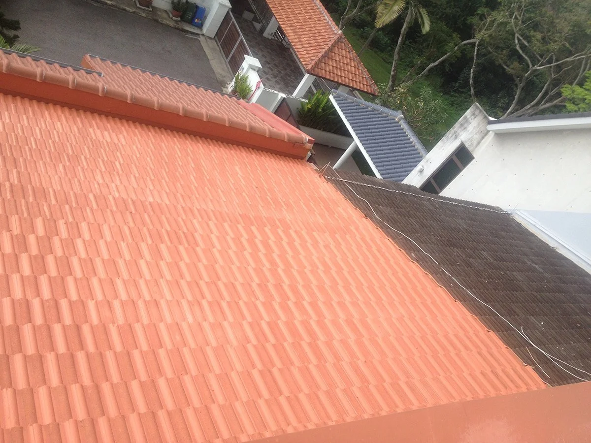 A view of rooftops in a residential area with tiled roofs, some in orange, blue, and black, surrounded by trees and greenery.