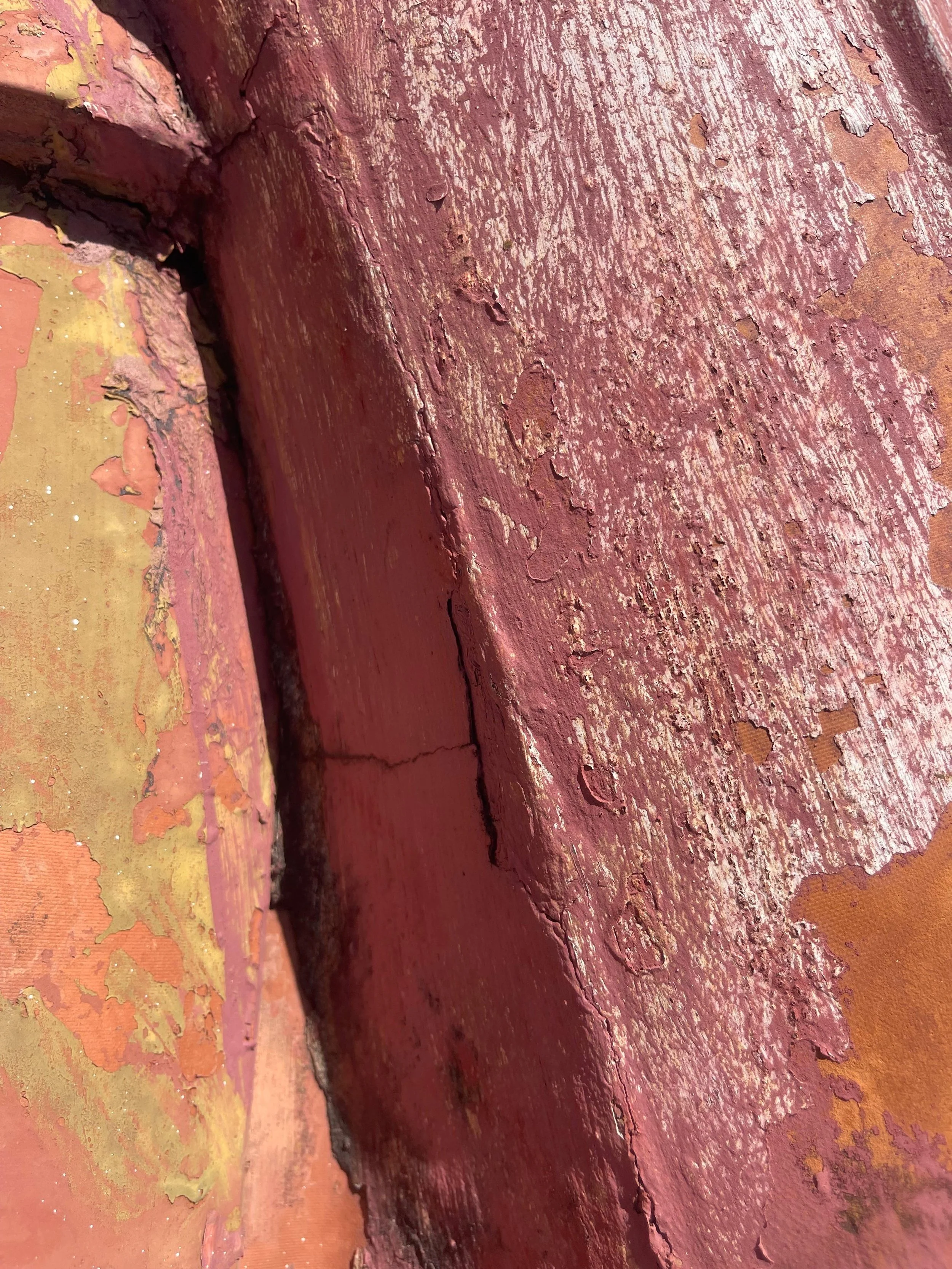 Close-up of weathered, peeling paint on a brick wall surface with cracks and chipped areas.