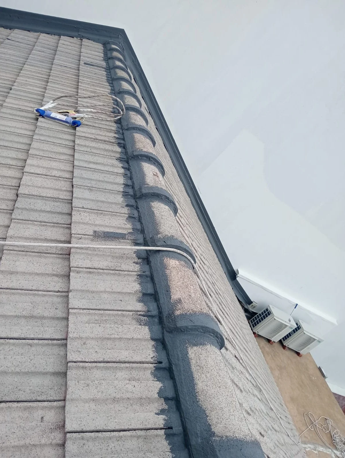 Rooftop with electrical wires and conduit along the edge of a corrugated roof, with HVAC units and a clear sky in the background.