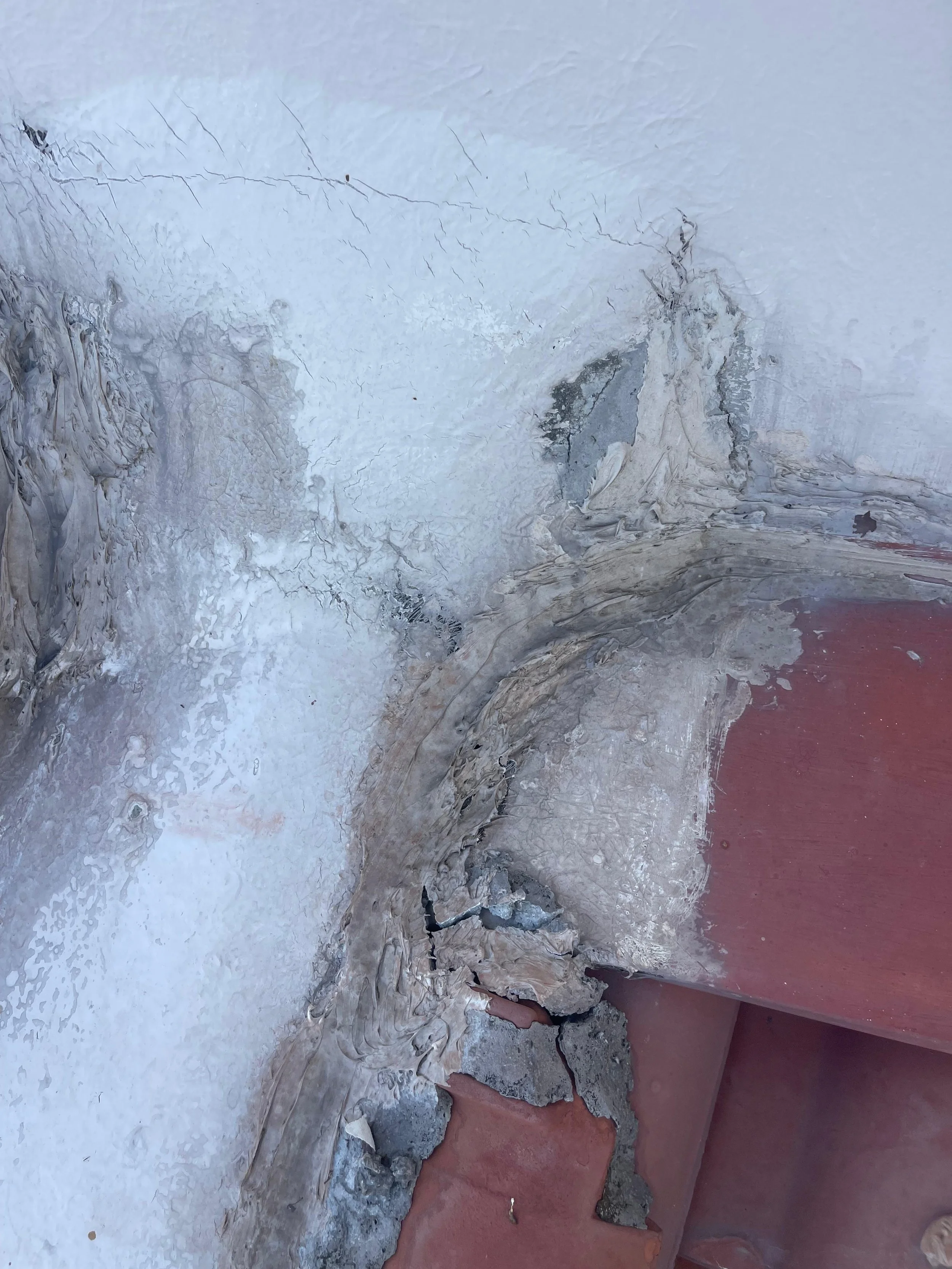 Cracked and peeling wall with damaged paint and plaster near a red-colored surface.