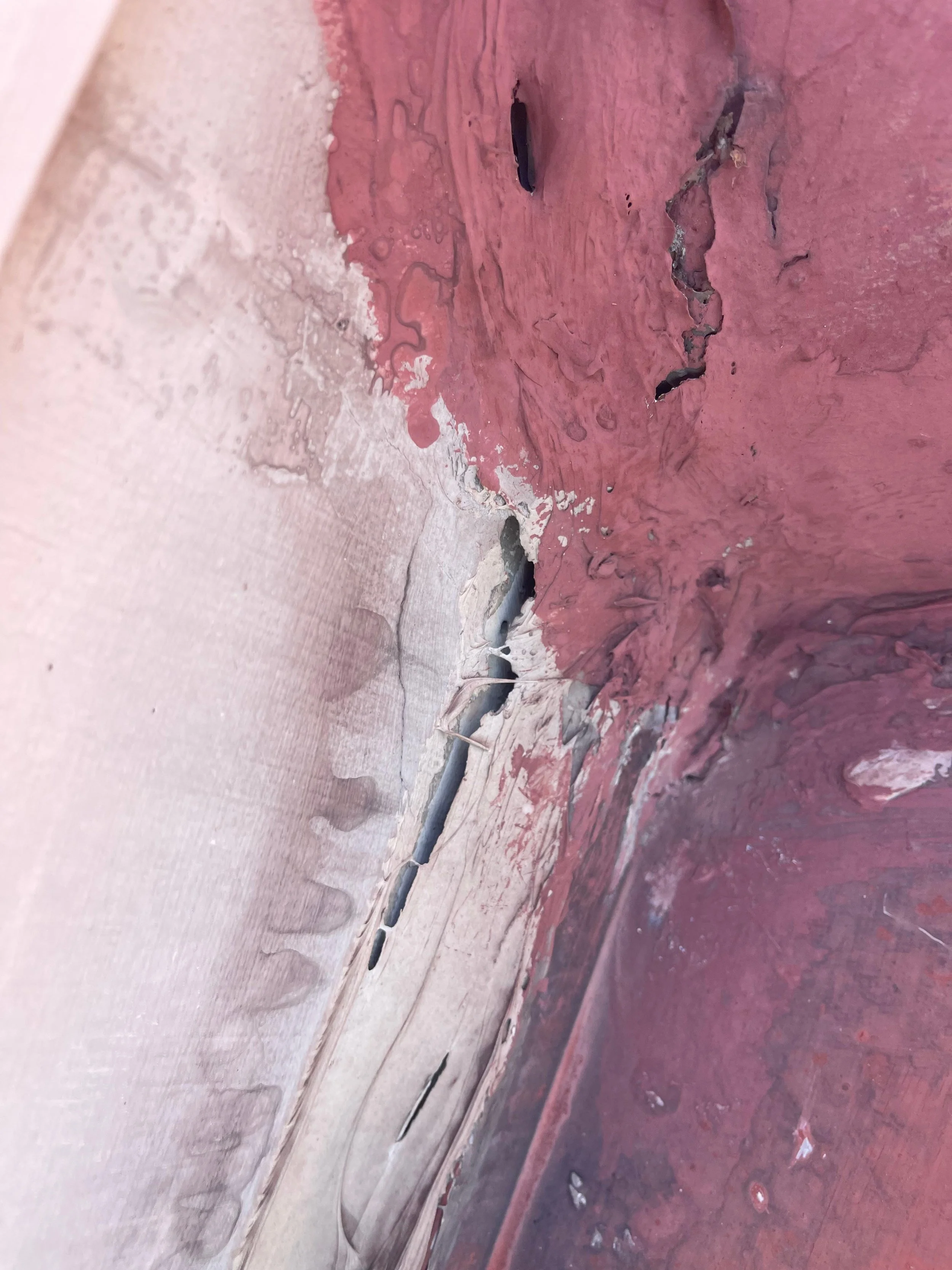 Close-up of a corner with peeling red and beige paint and exposed cracks.