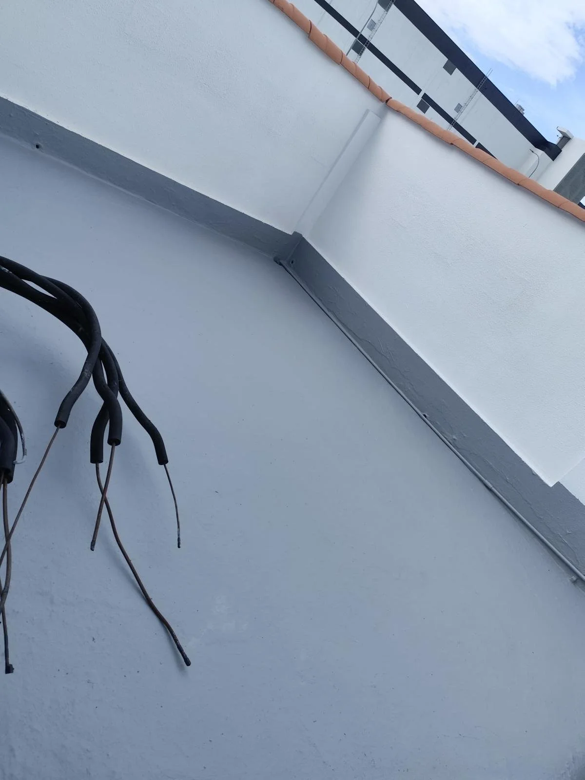 Wires and cables on a white balcony floor with a white wall and a small section of the roof visible.