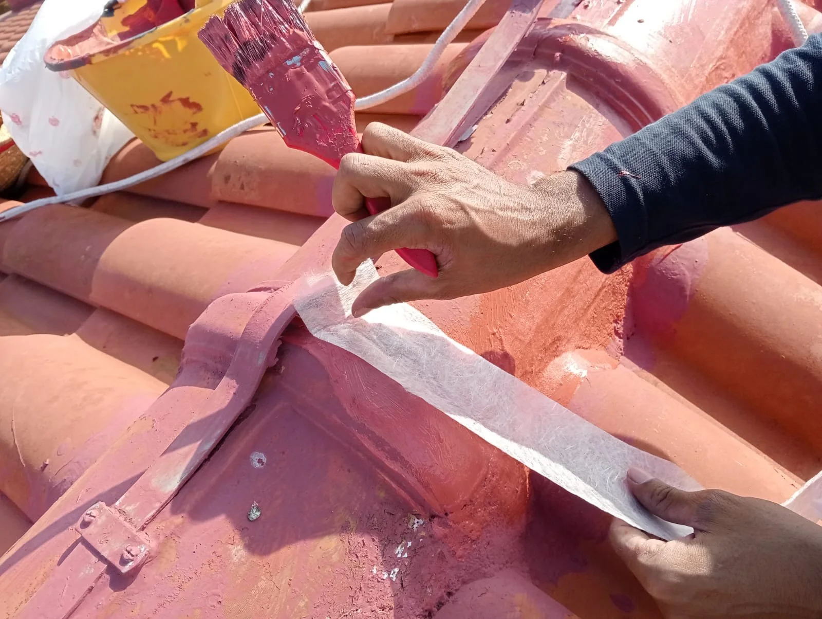 Close-up of a worker painting or sealing the edge of a roof with pink-colored paint or sealant, using a small paintbrush or applicator.