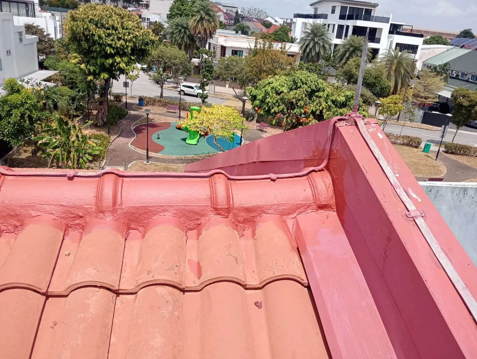 View from a rooftop showing a small park with a playground, trees, benches, and surrounding residential buildings and streets.