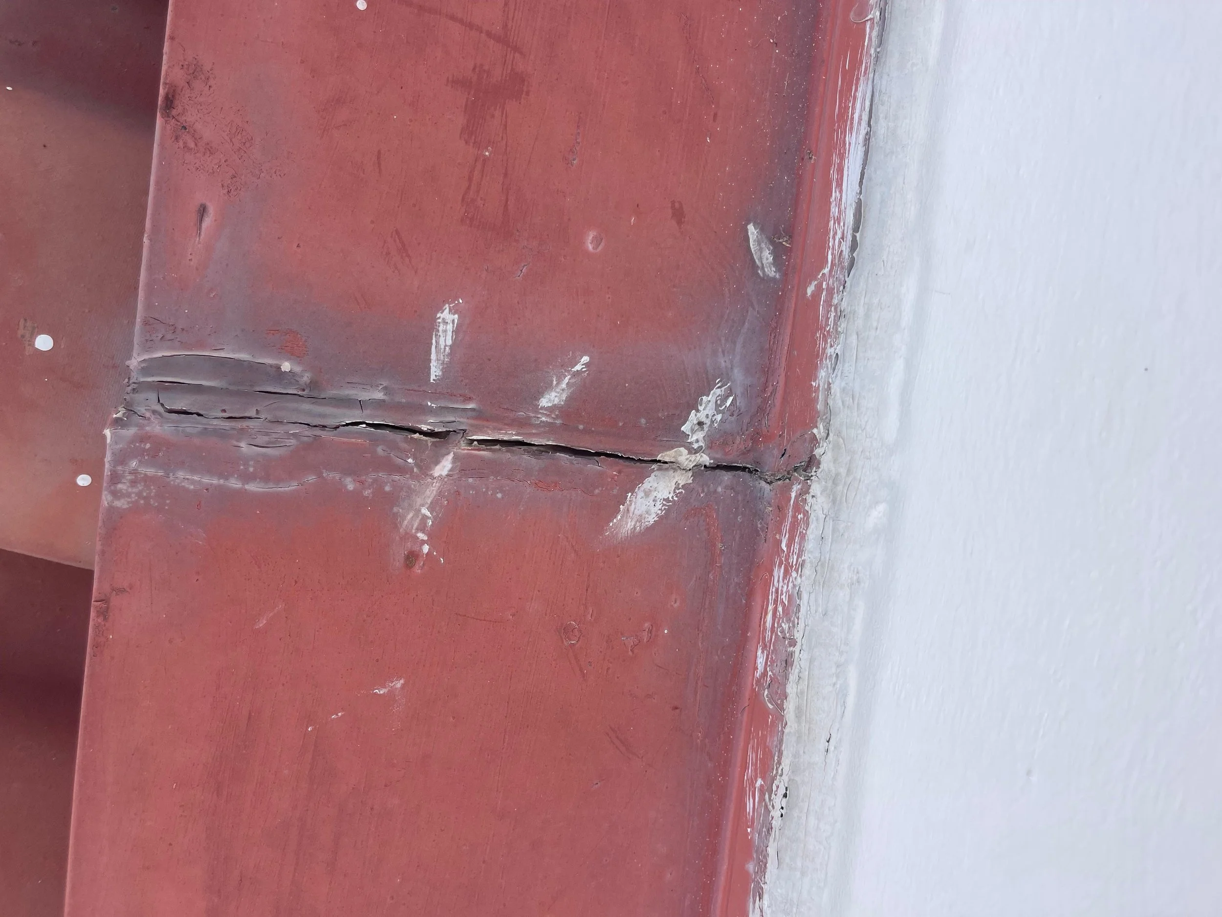 Close-up of a corner where red wall meets white wall, showing a large crack and damage in the red paint and underlying material.