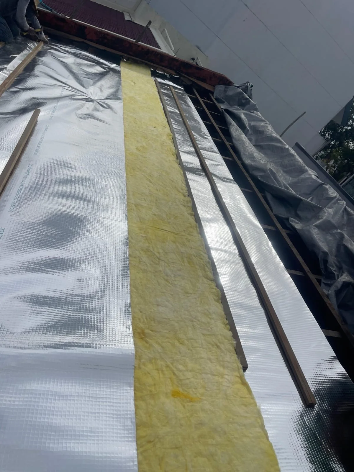 Roof under construction with reflective insulation, yellow fiberglass insulation, and wooden battens.