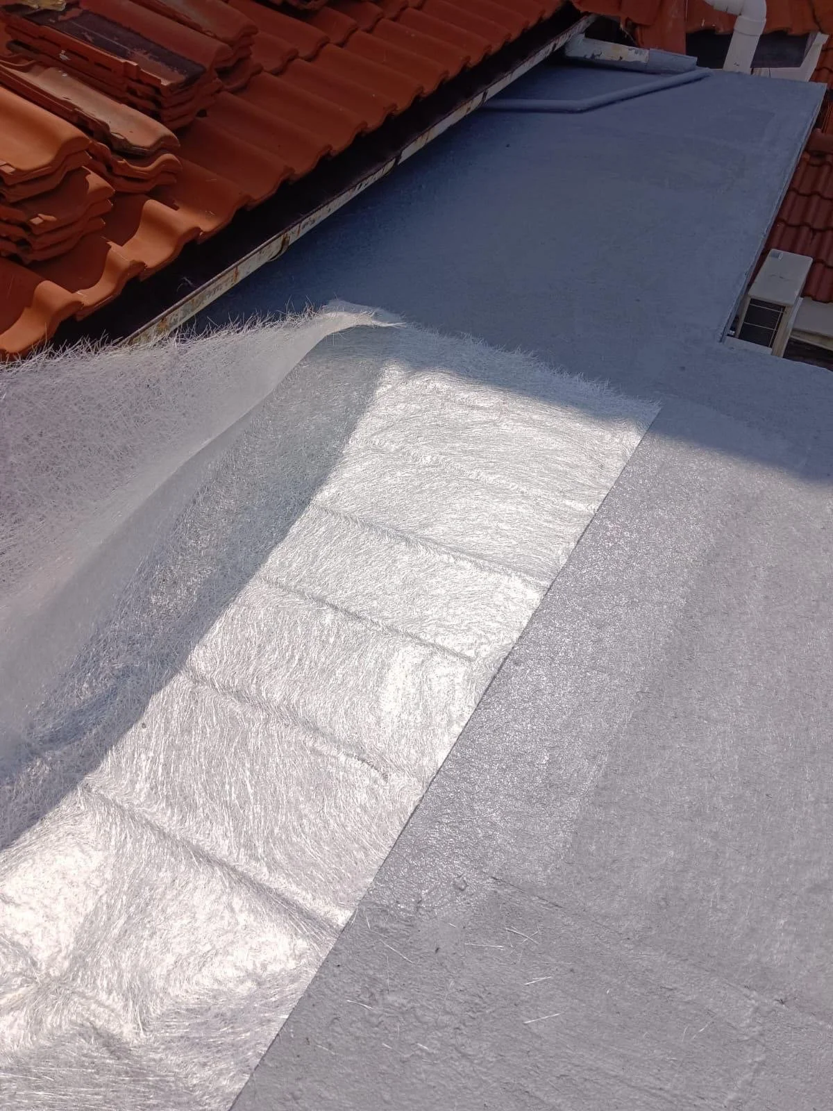 Close-up of a roof with red clay tiles, blue roofing material, and a section of reflective silver insulation or waterproofing membrane.