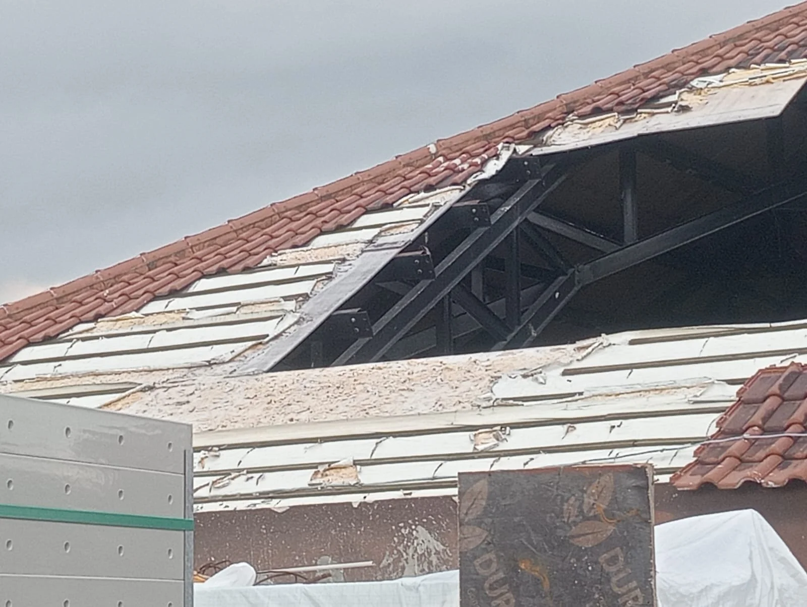 Roof under construction with partially installed white tiles and a red tiled section, showing black metal support structure underneath.