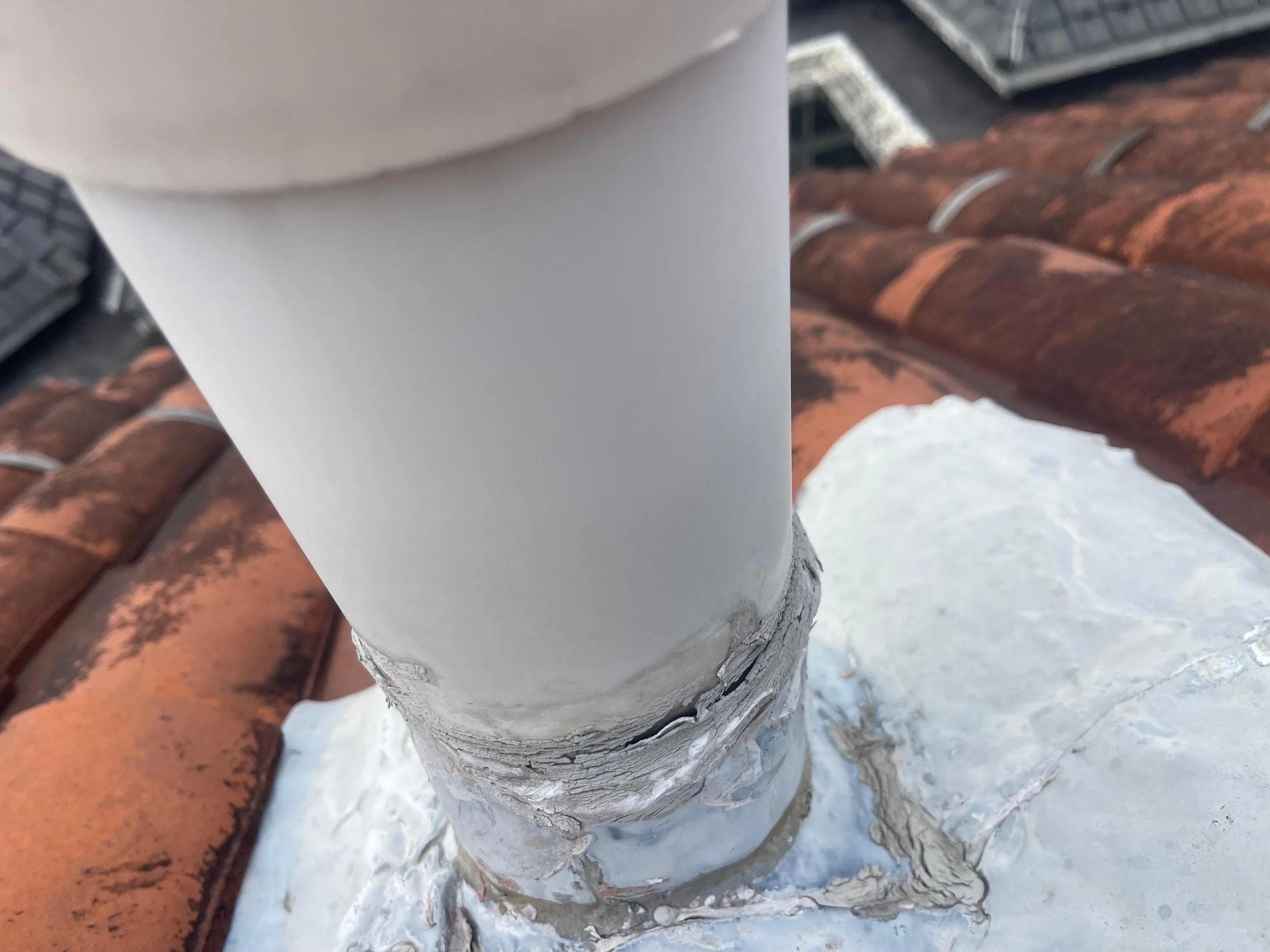 Close-up of a white chimney pipe emerging from a metal flashing on a tiled roof.