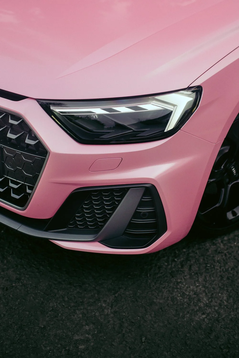 Close-up of the front of a pink car, showing the headlight, grille, and bumper.