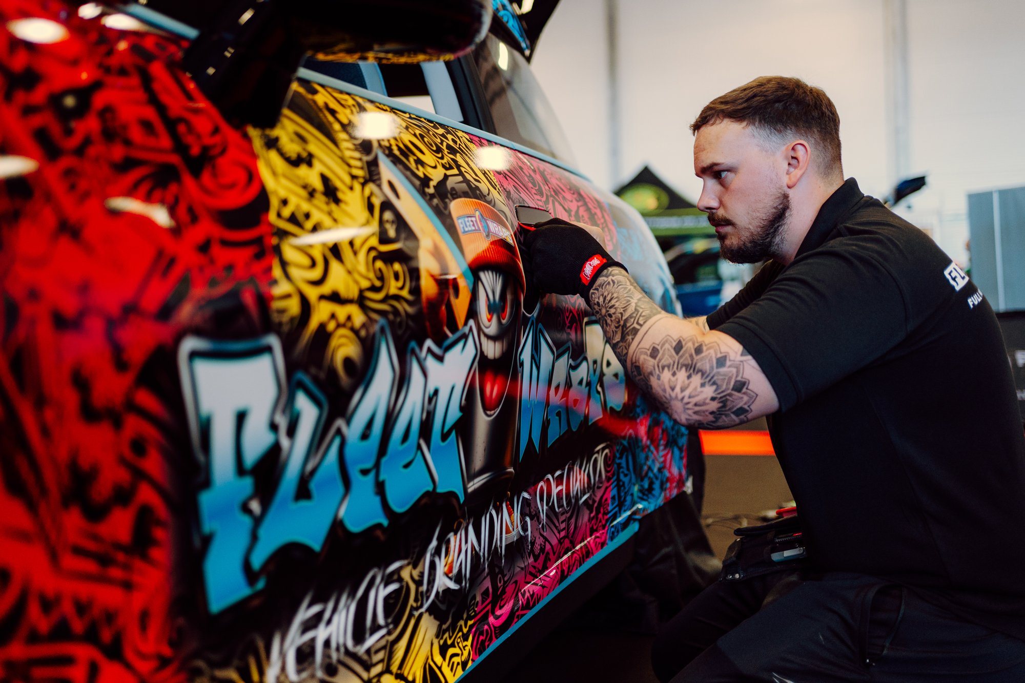 A man with tattoos working on a colorful race car with graffiti-style designs in a garage or workshop.